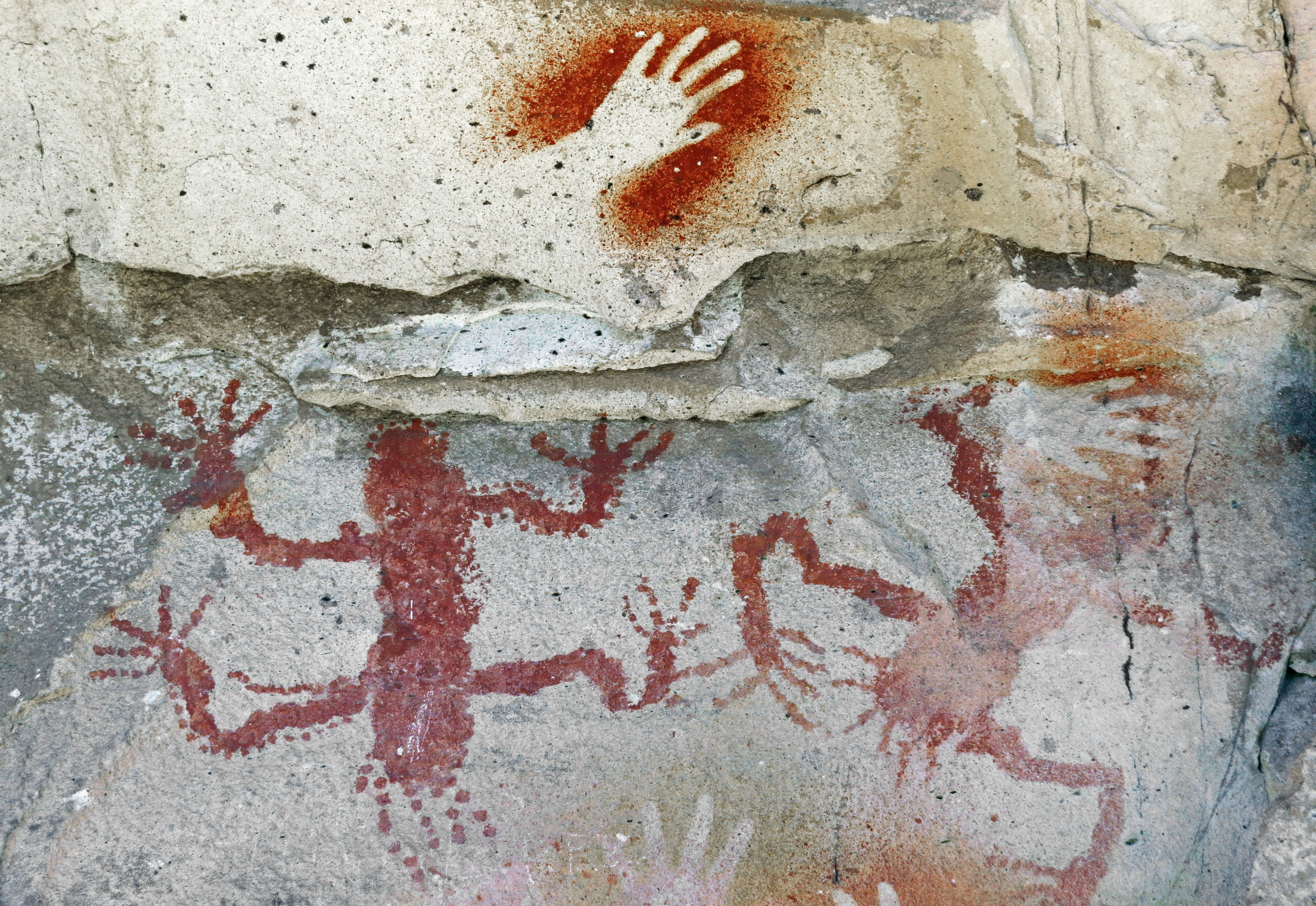 Ancient cave paintings featuring handprints and human-like figures