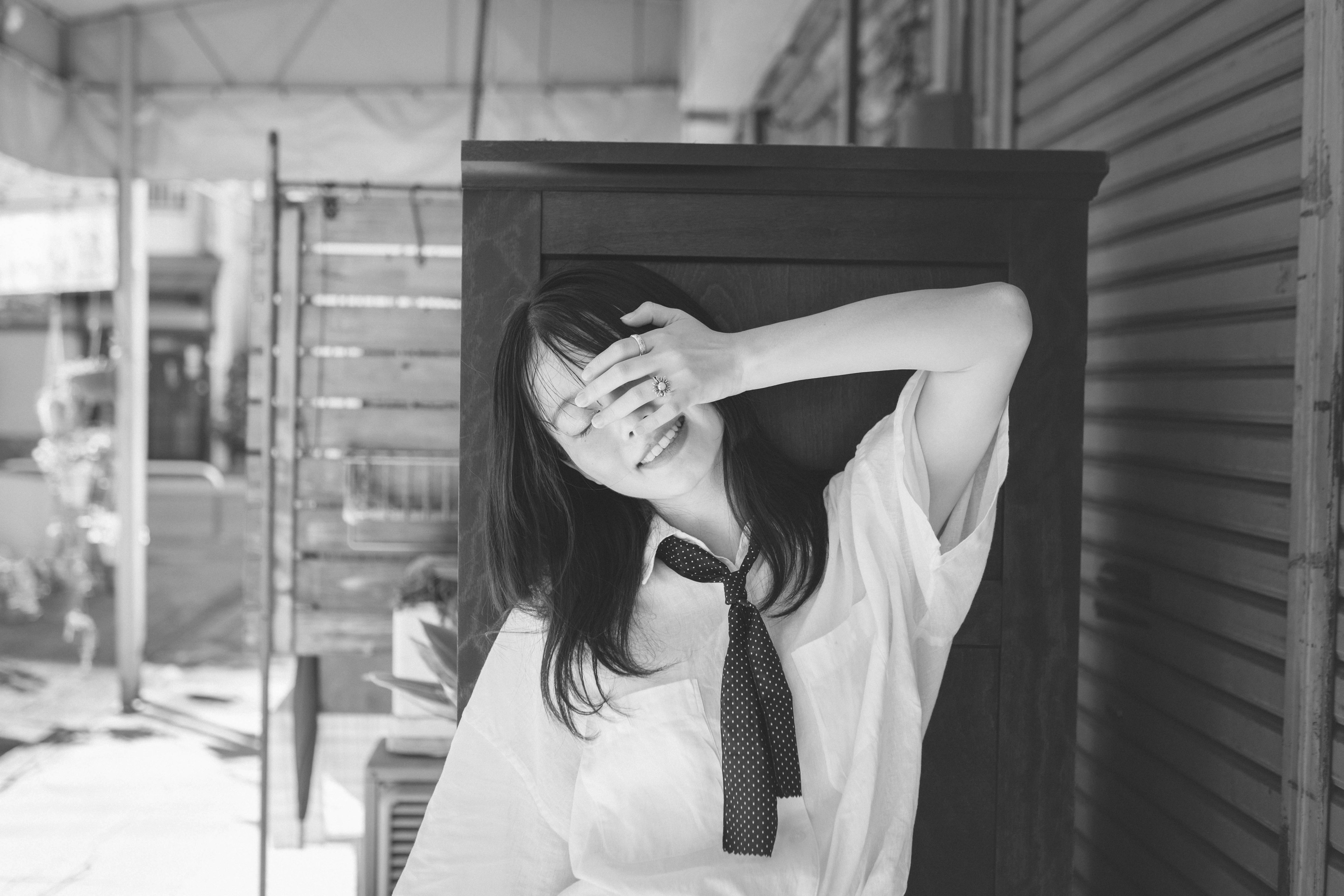 Una mujer sonriendo mientras cubre su rostro con la mano en un entorno en blanco y negro