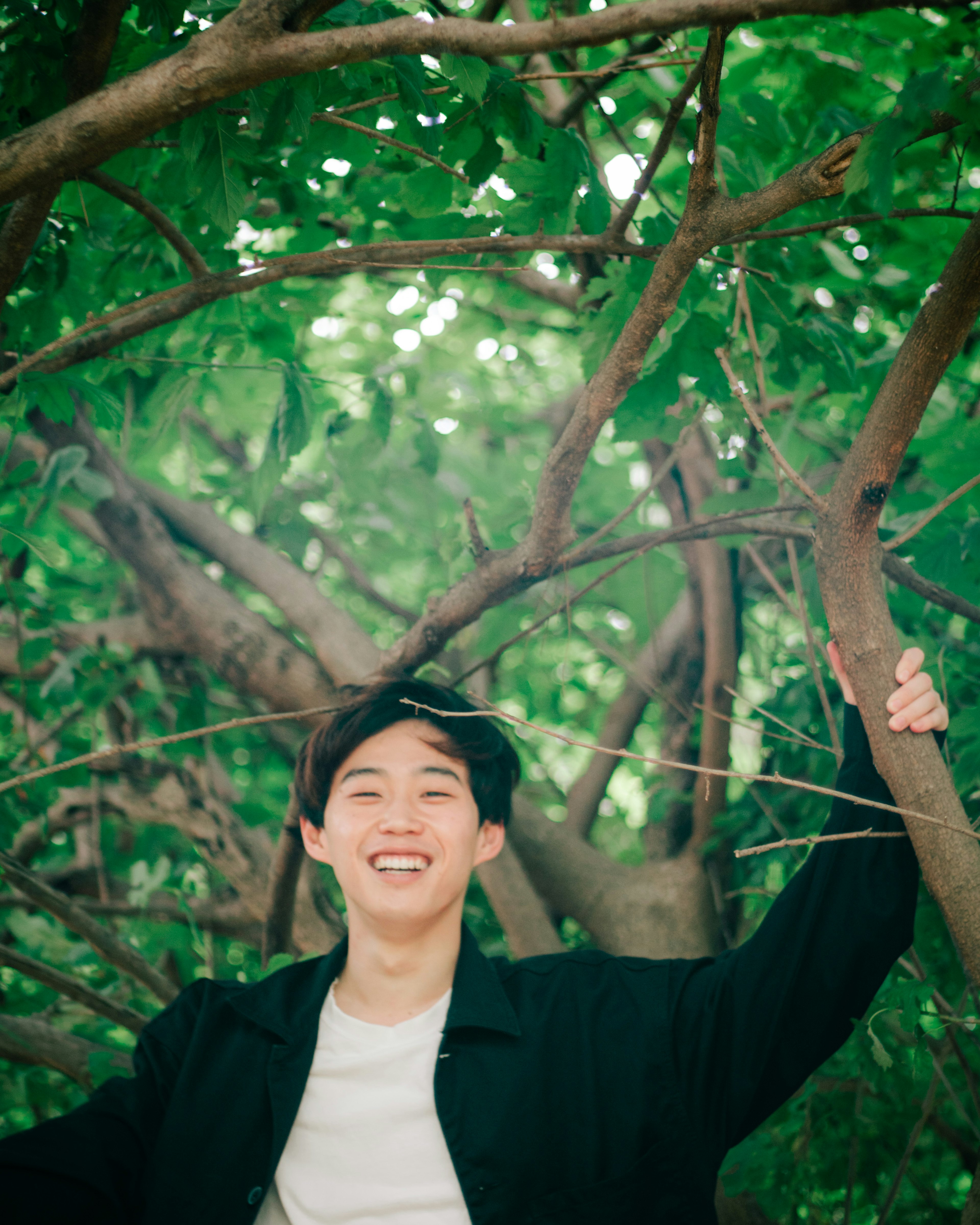 Jeune homme souriant joyeusement parmi des arbres verts