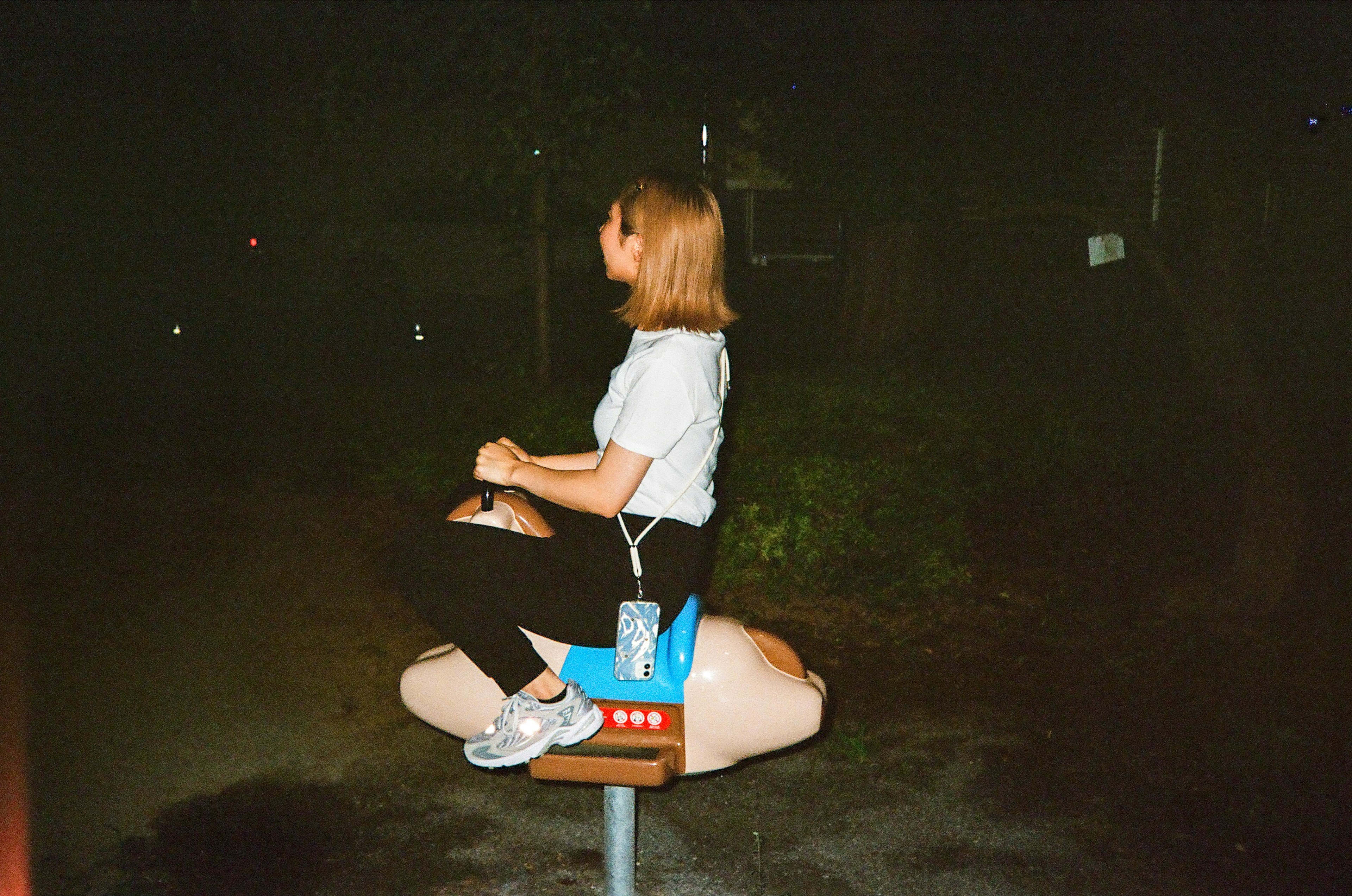 A woman sitting on a playground ride at night