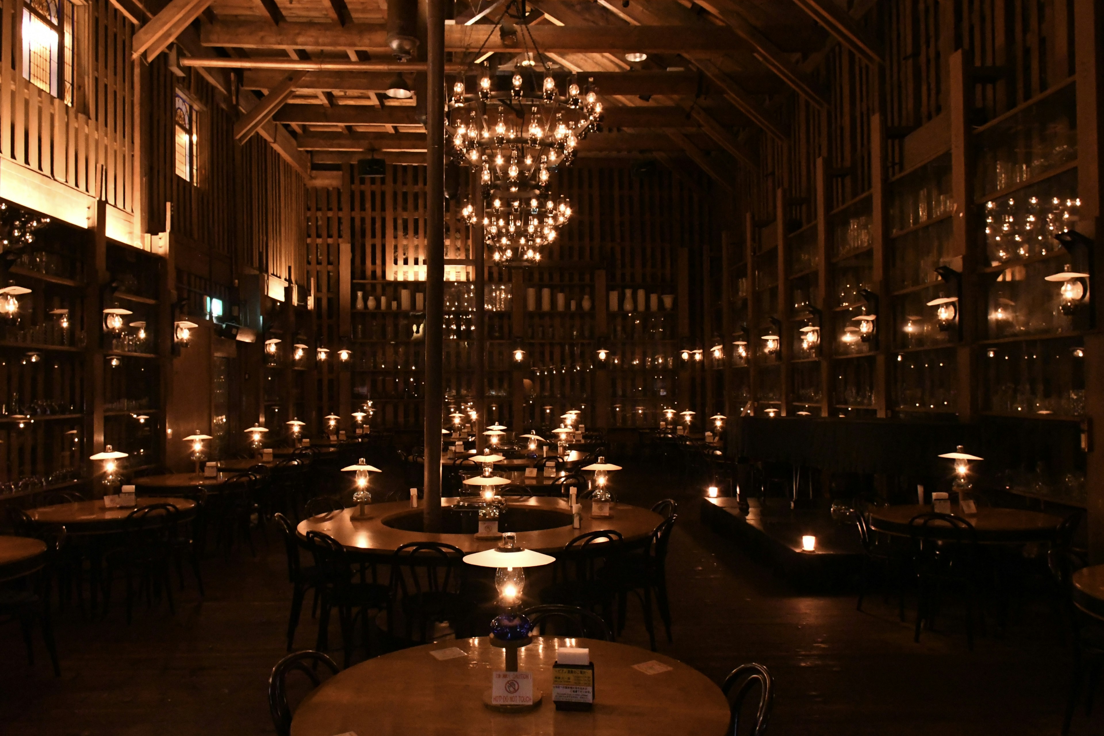 A dimly lit restaurant with wooden interior featuring candlelit tables and impressive chandeliers