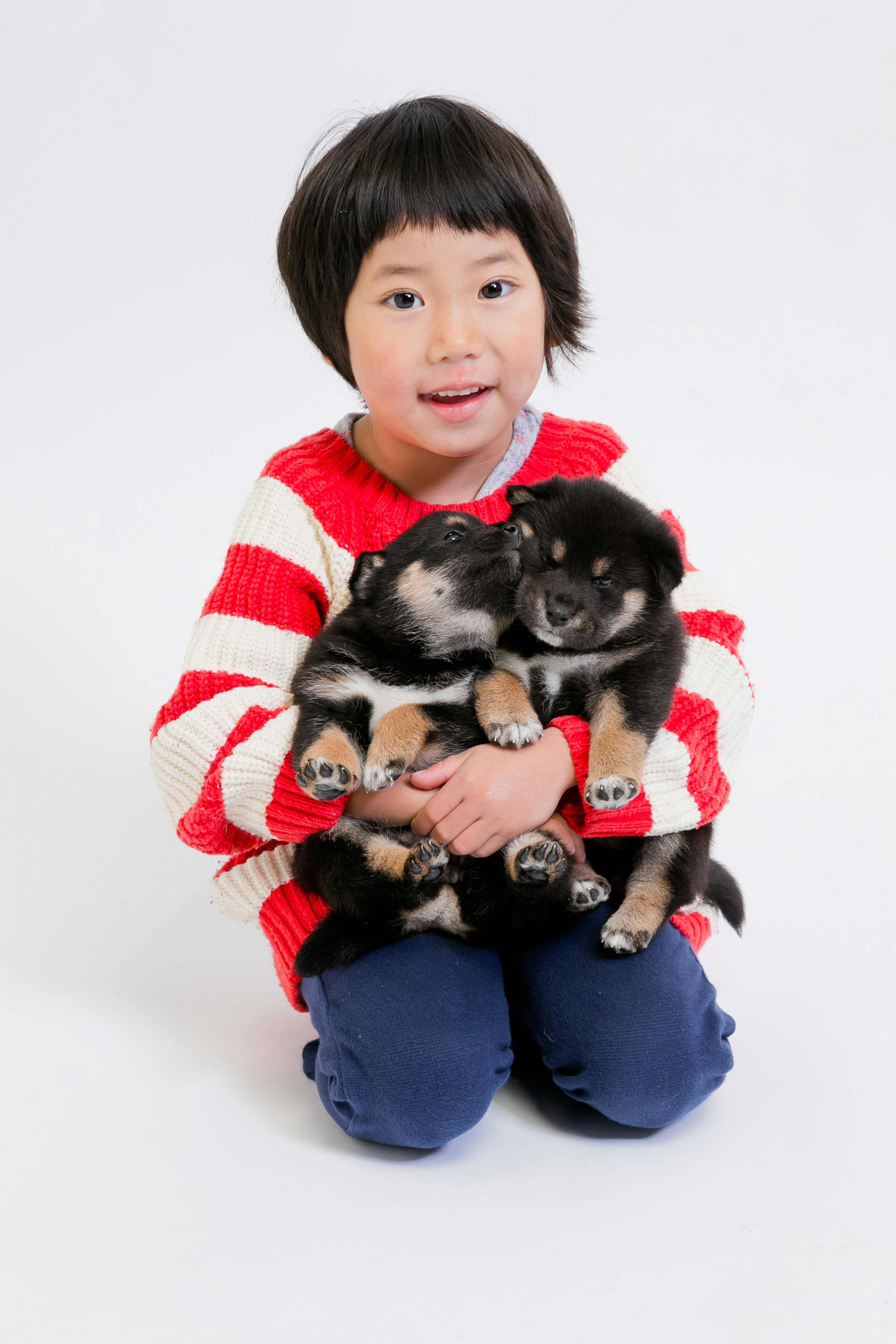 A child in a red striped sweater holding two puppies