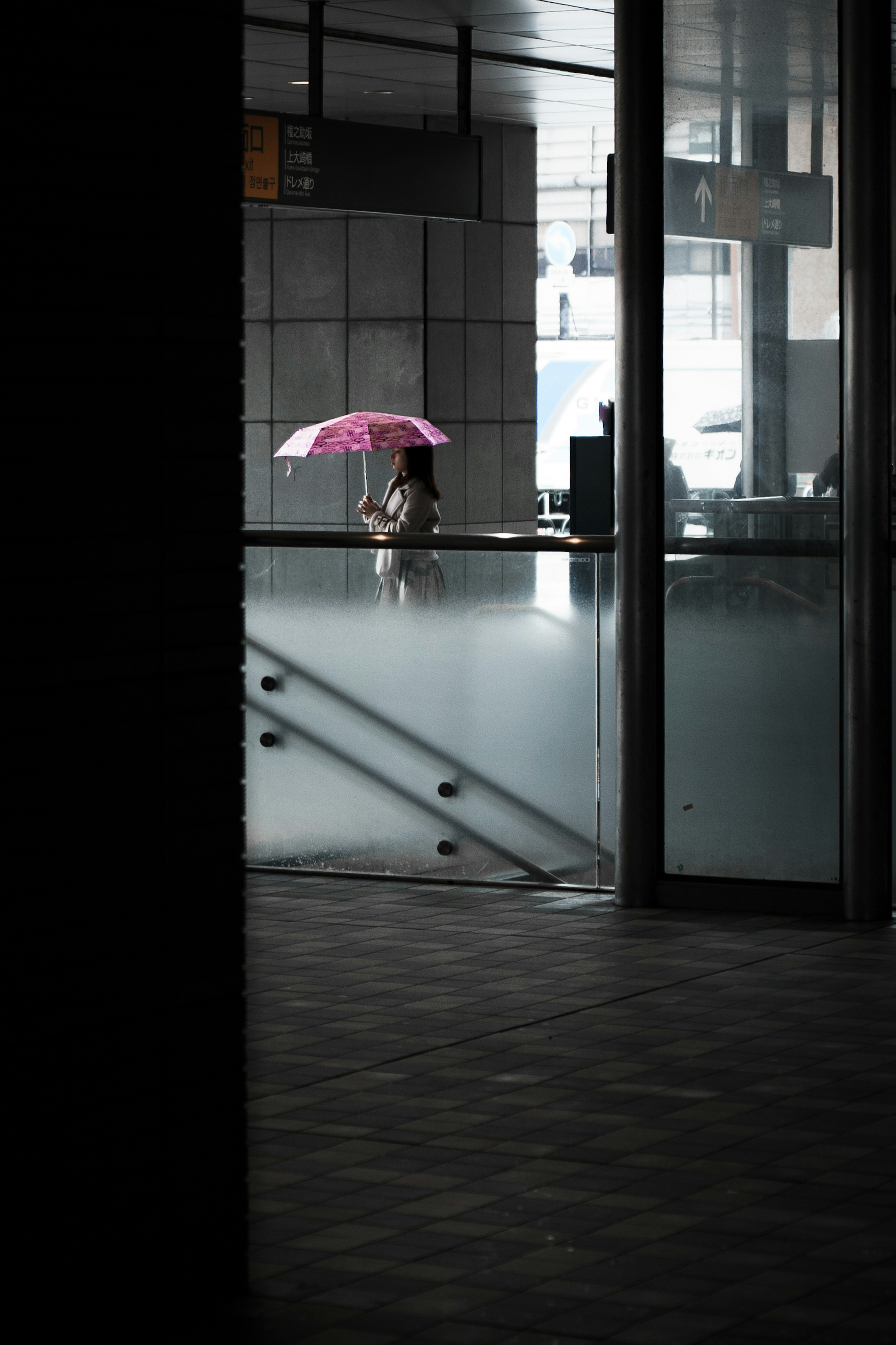 薄暗い空間に立つ女性の後ろ姿とピンクの傘