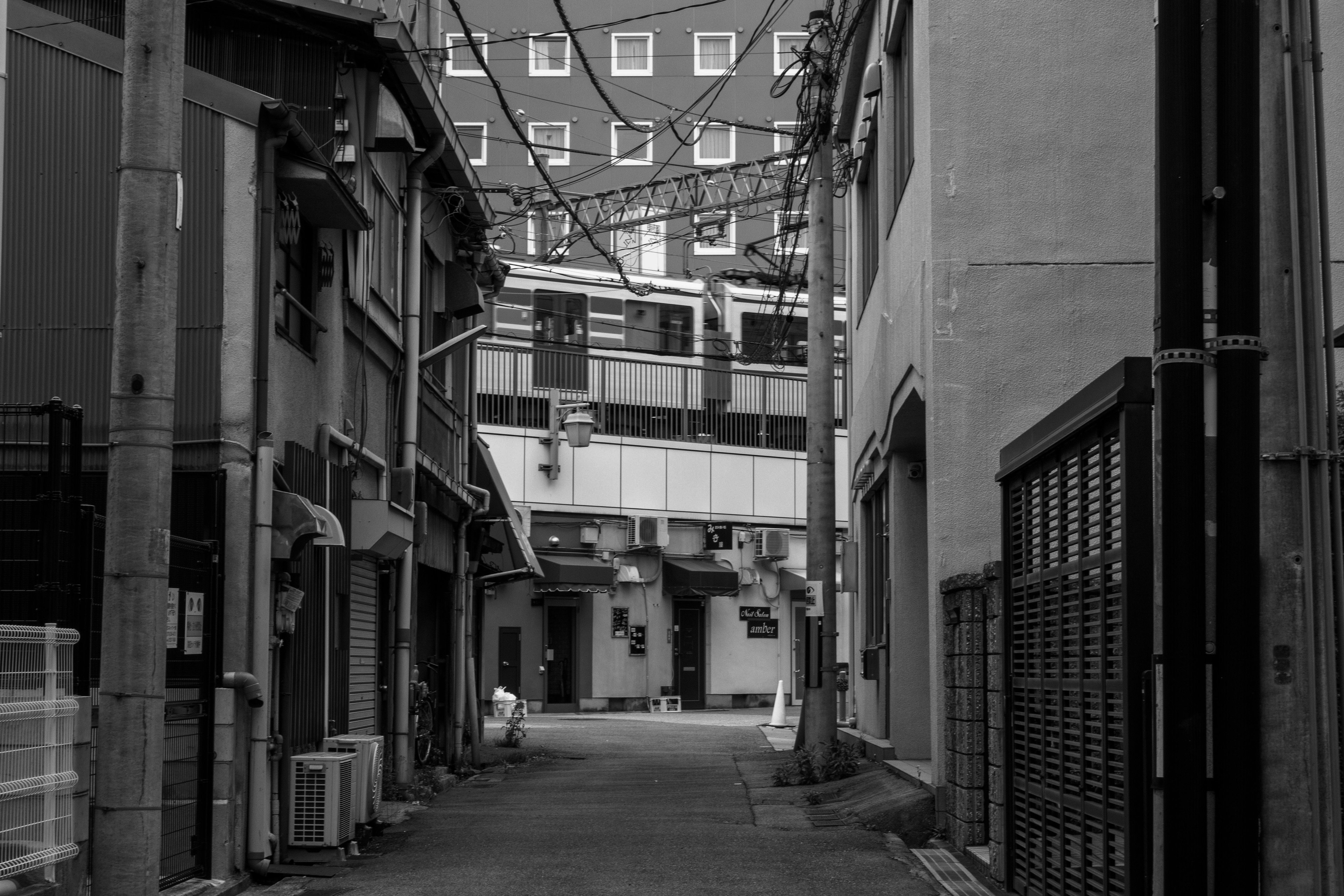 Black and white view of narrow alley with buildings and an elevated train