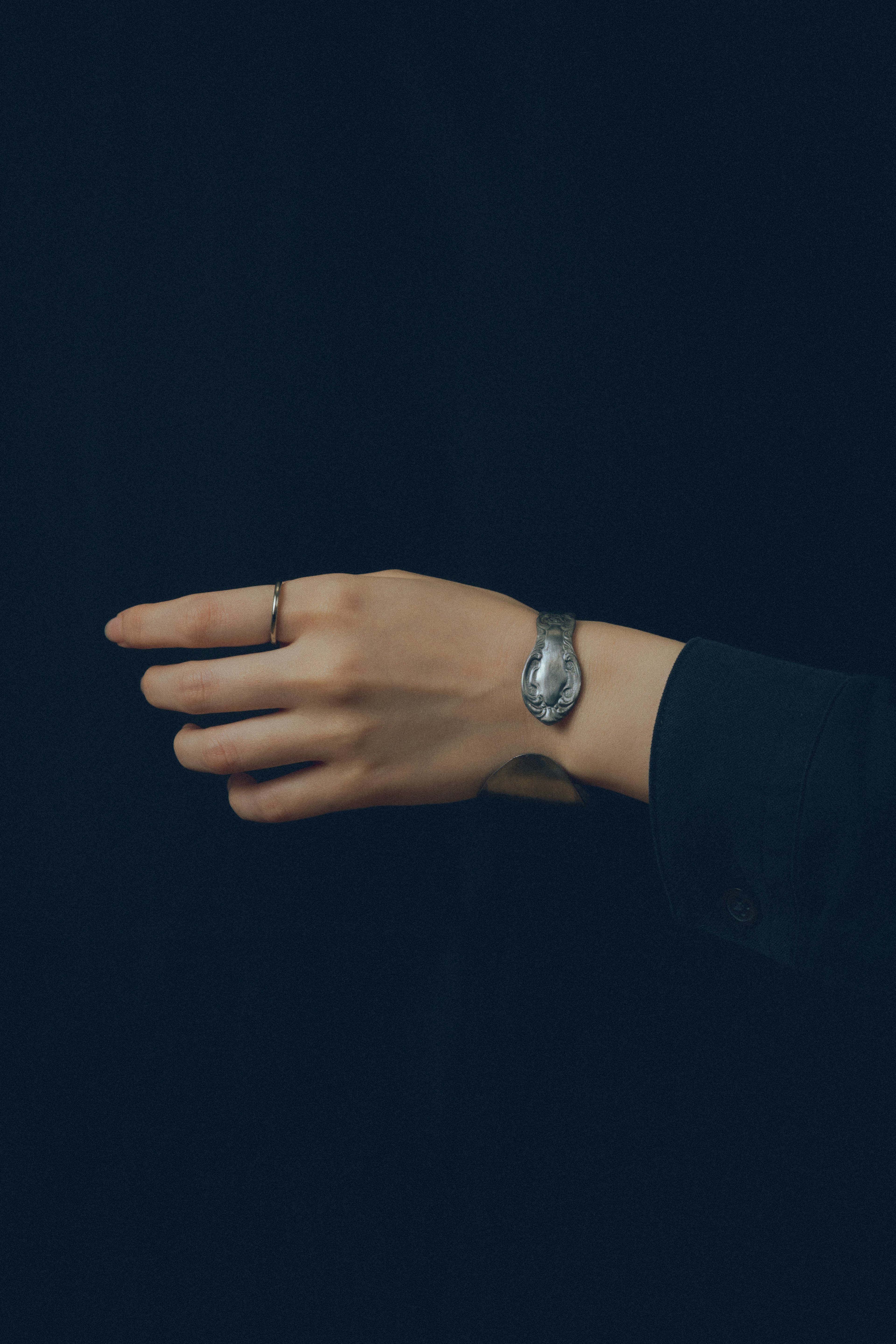 A hand with a silver watch is reaching out against a dark background