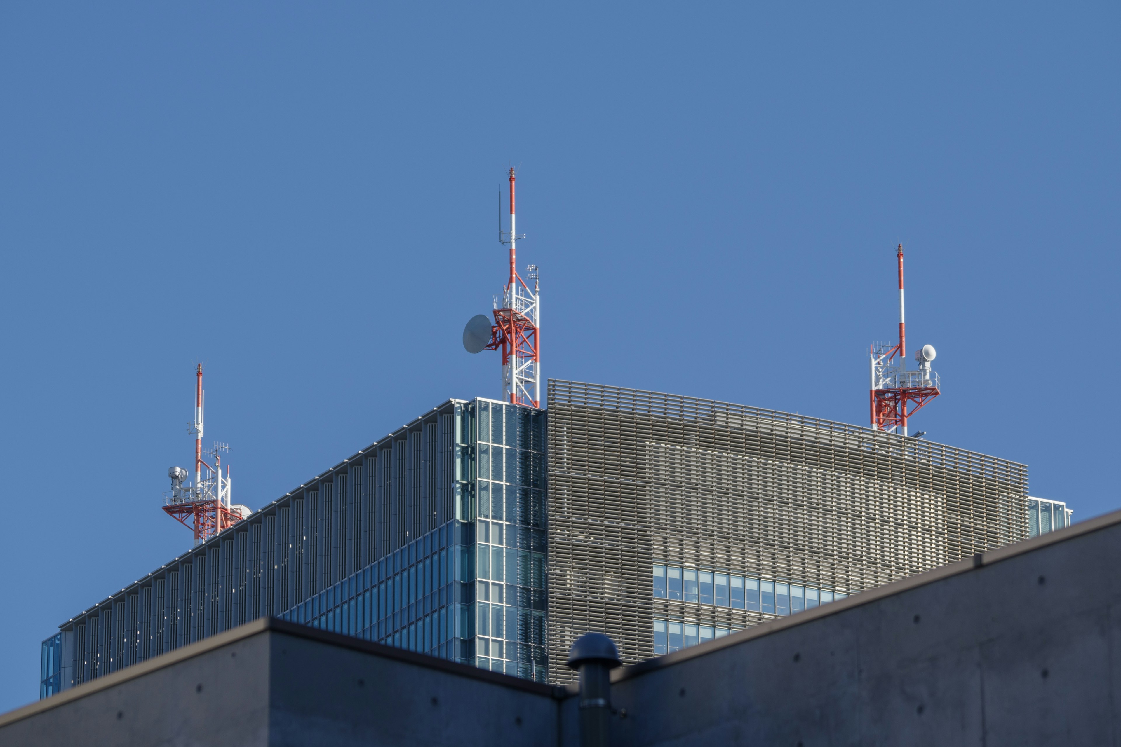 Bâtiment moderne surmonté d'antennes rouges et blanches sous un ciel bleu clair