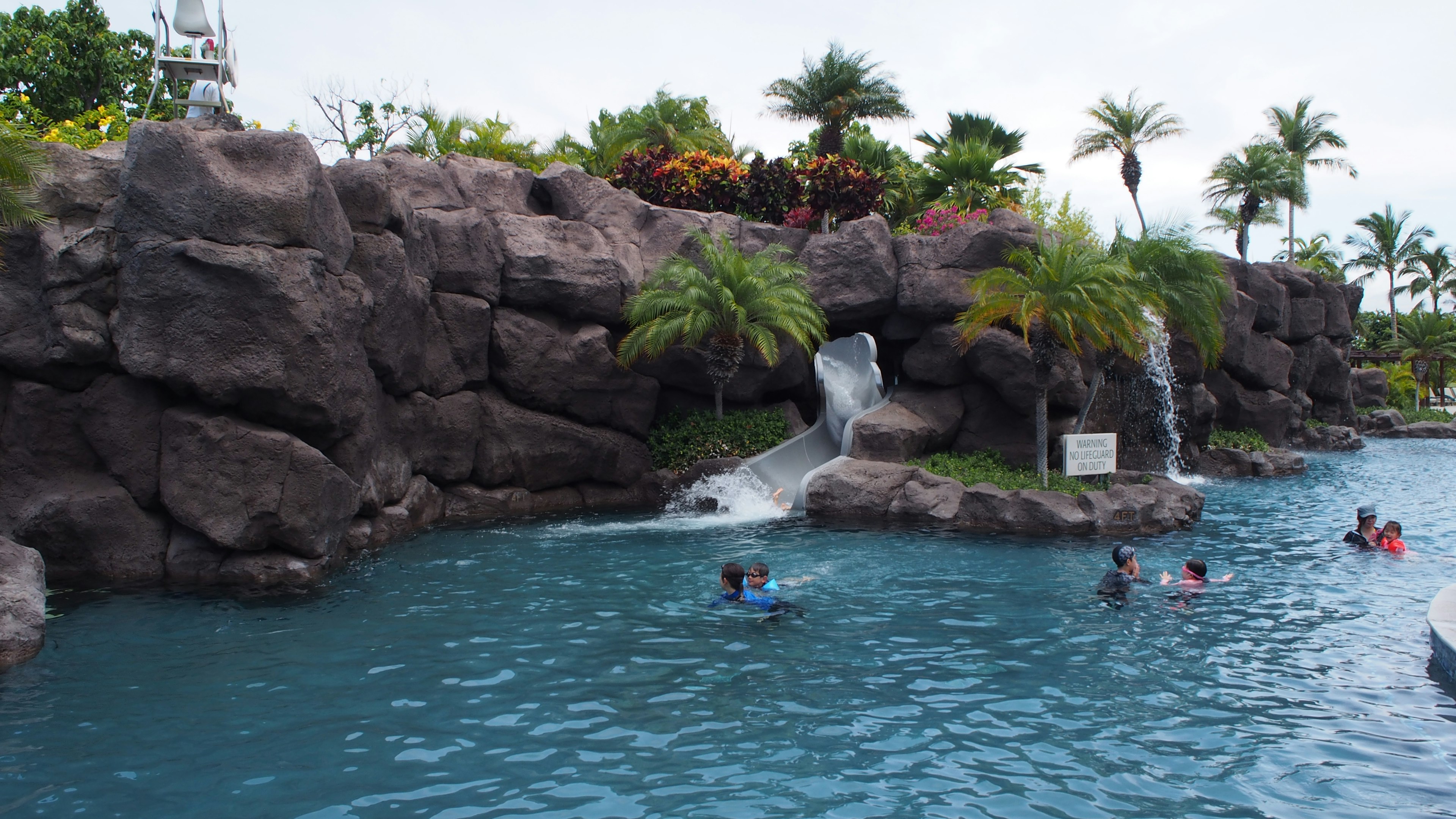 Resort scene with a blue pool and waterfall featuring people enjoying the water