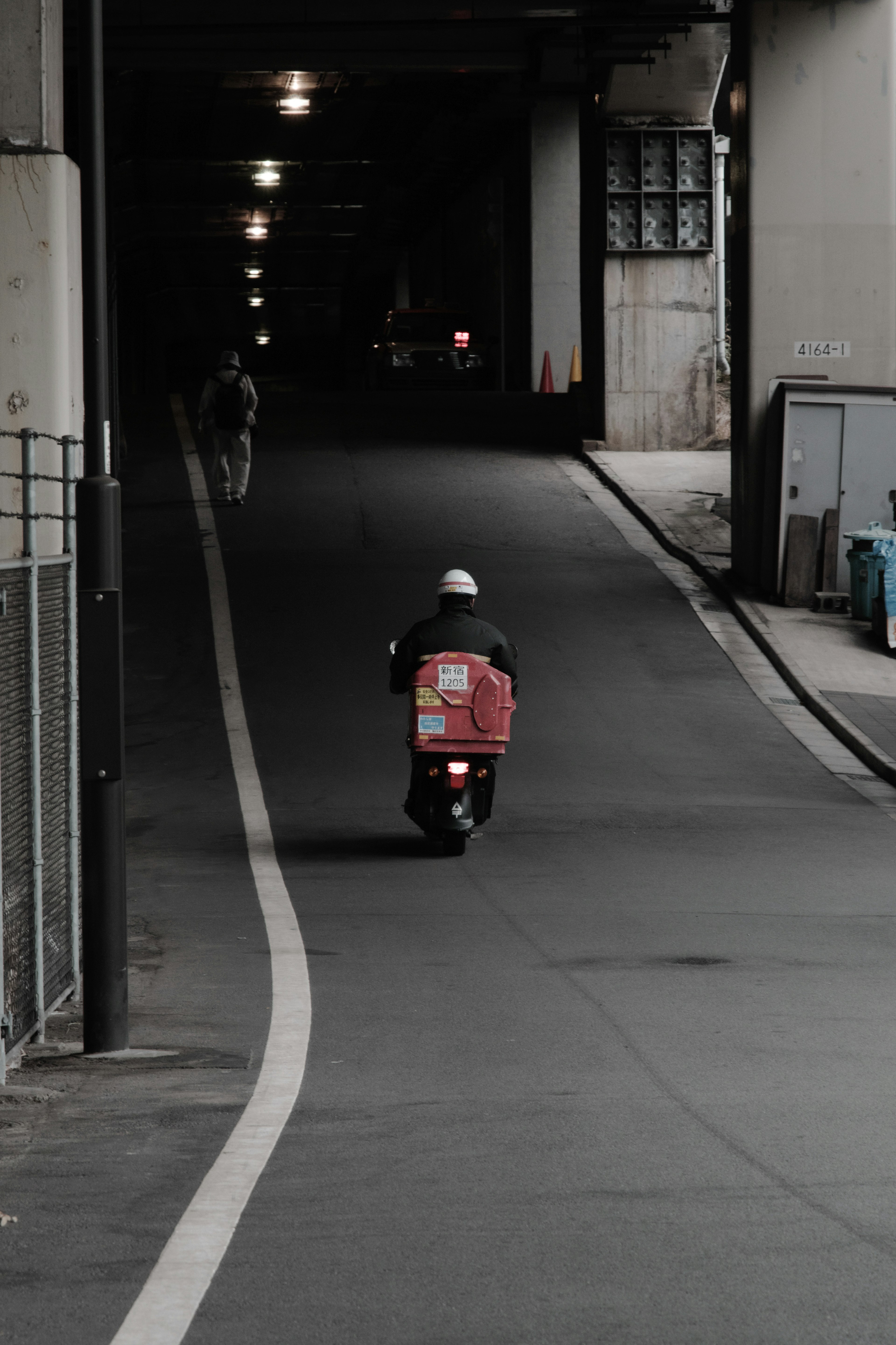 Lieferfahrer auf einem roten Roller, der durch einen dunklen Tunnel fährt