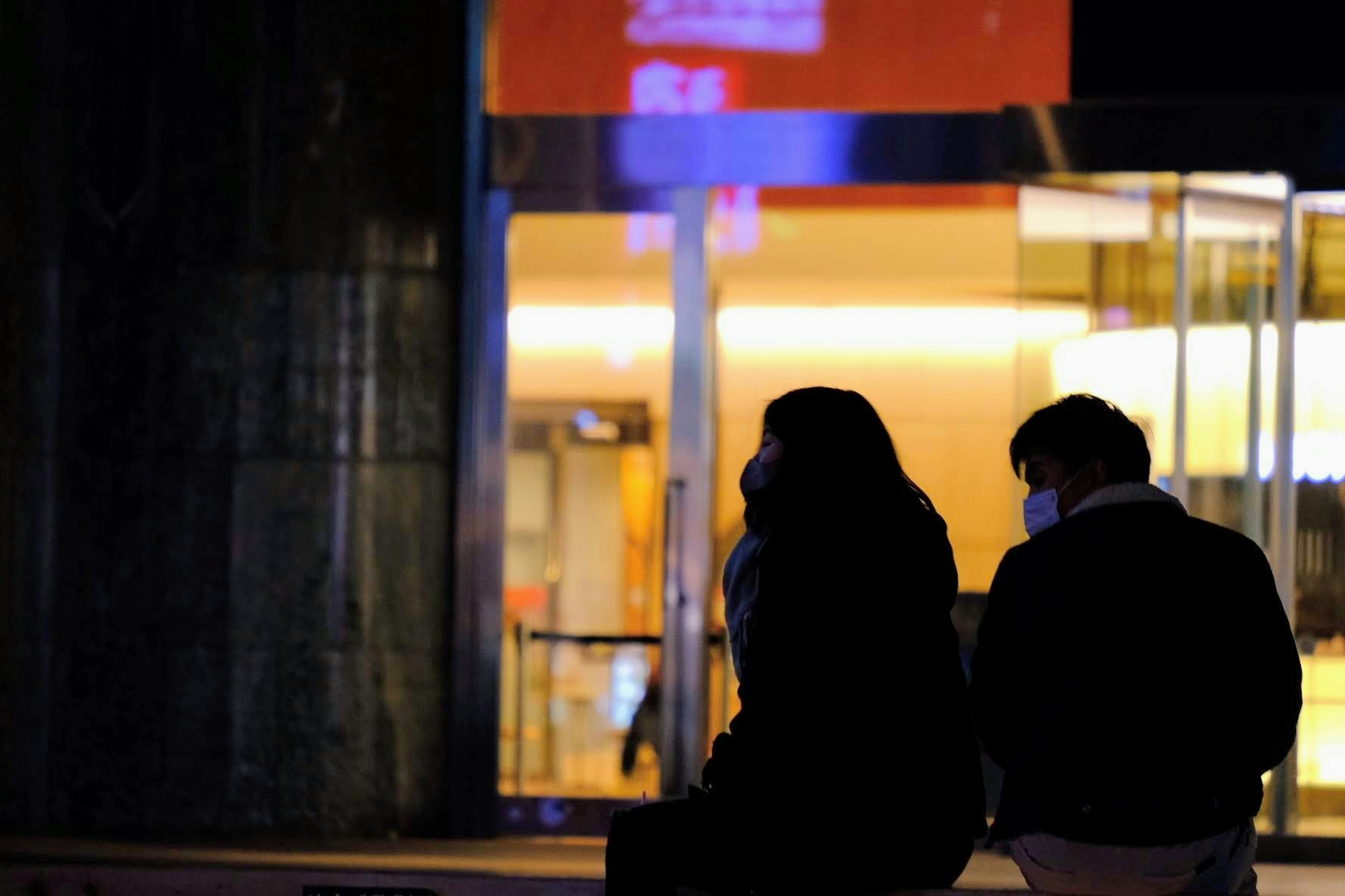 Silhouette of a couple sitting in front of a stylish store at night