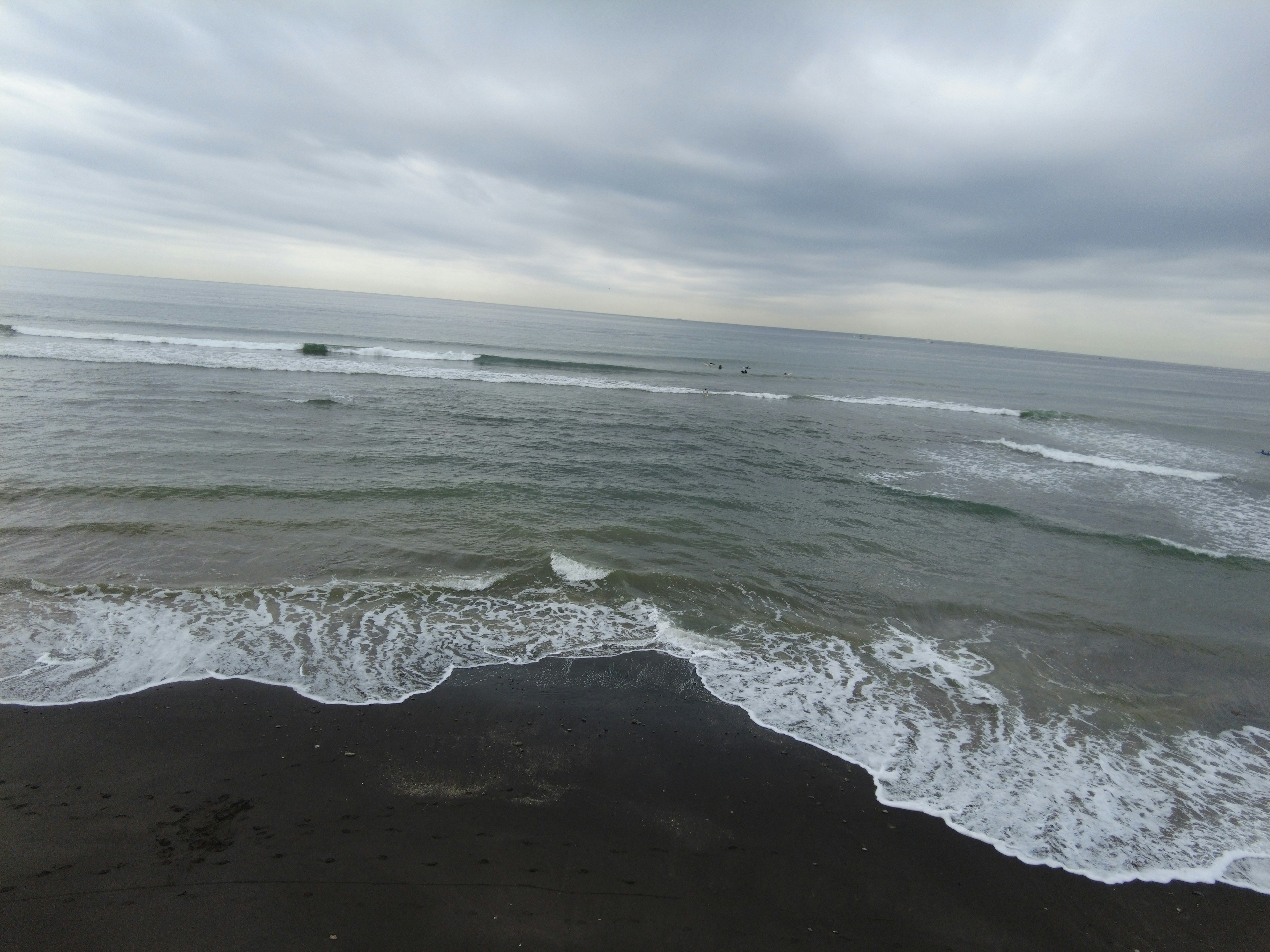 Onde che si infrangono su una spiaggia di sabbia scura sotto un cielo nuvoloso