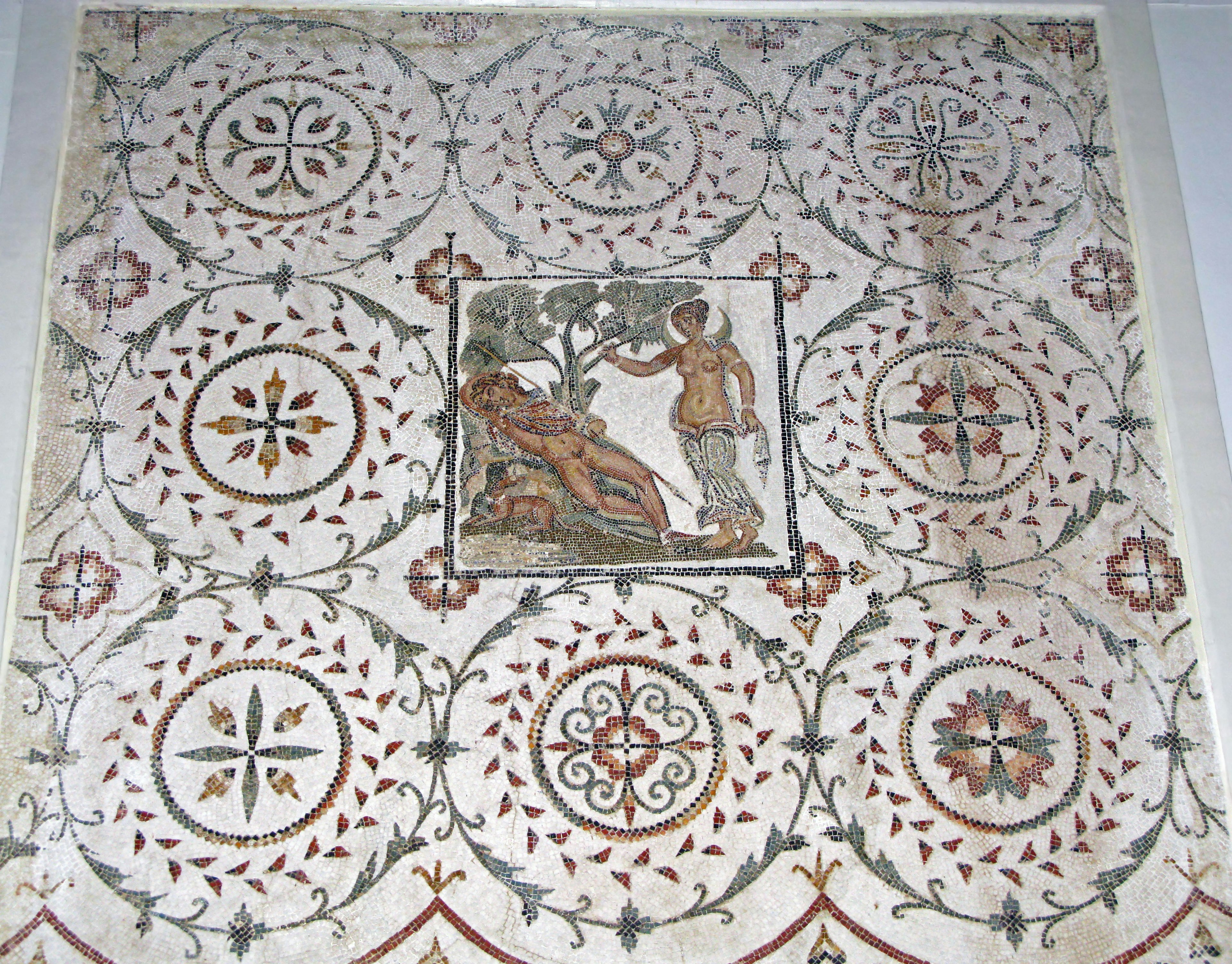 Ancient mosaic floor design featuring a central figure with plants surrounded by geometric patterns