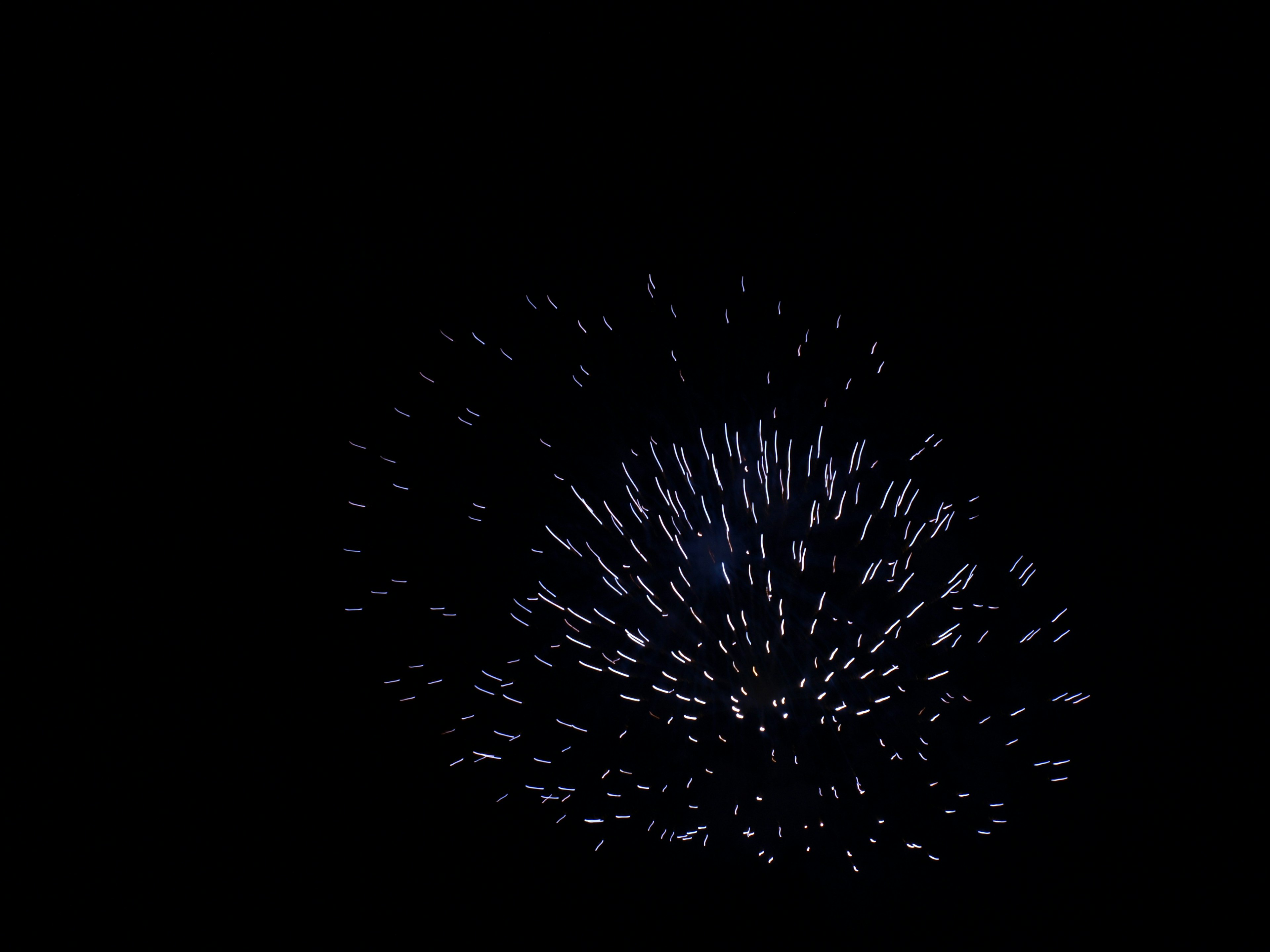 Fuegos artificiales estallando en un patrón azul-blanco sobre un fondo negro