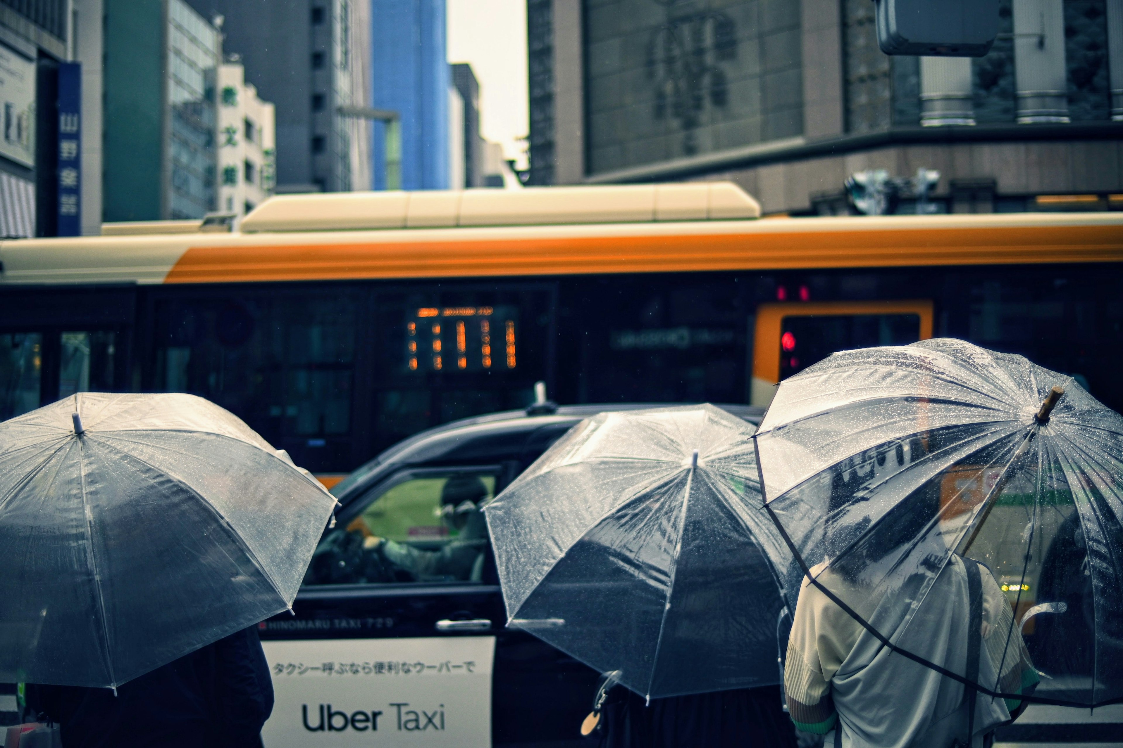 Urban scene with people holding umbrellas and an Uber taxi in the rain