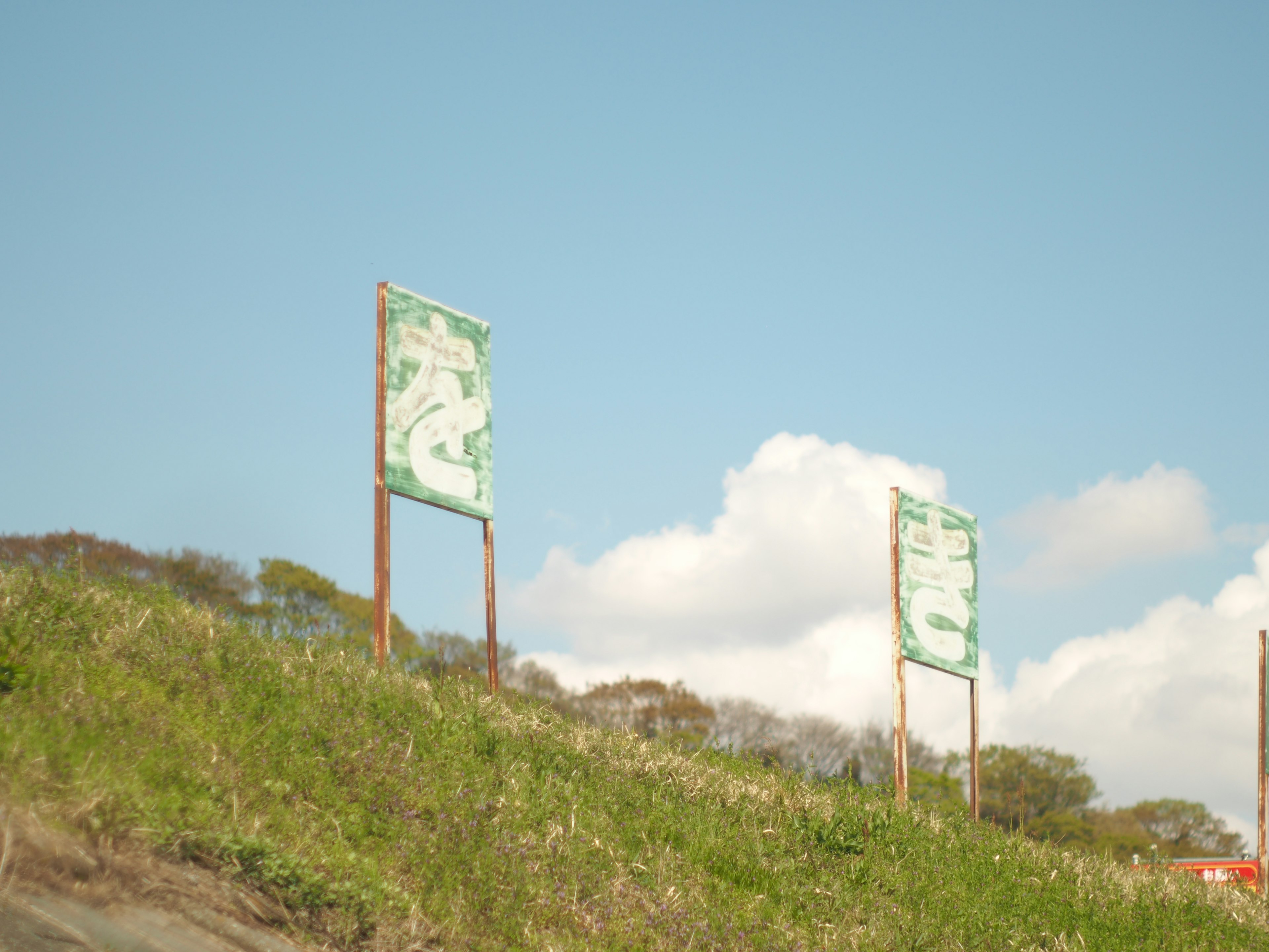 Dos letreros verdes en una colina cubierta de hierba bajo un cielo azul