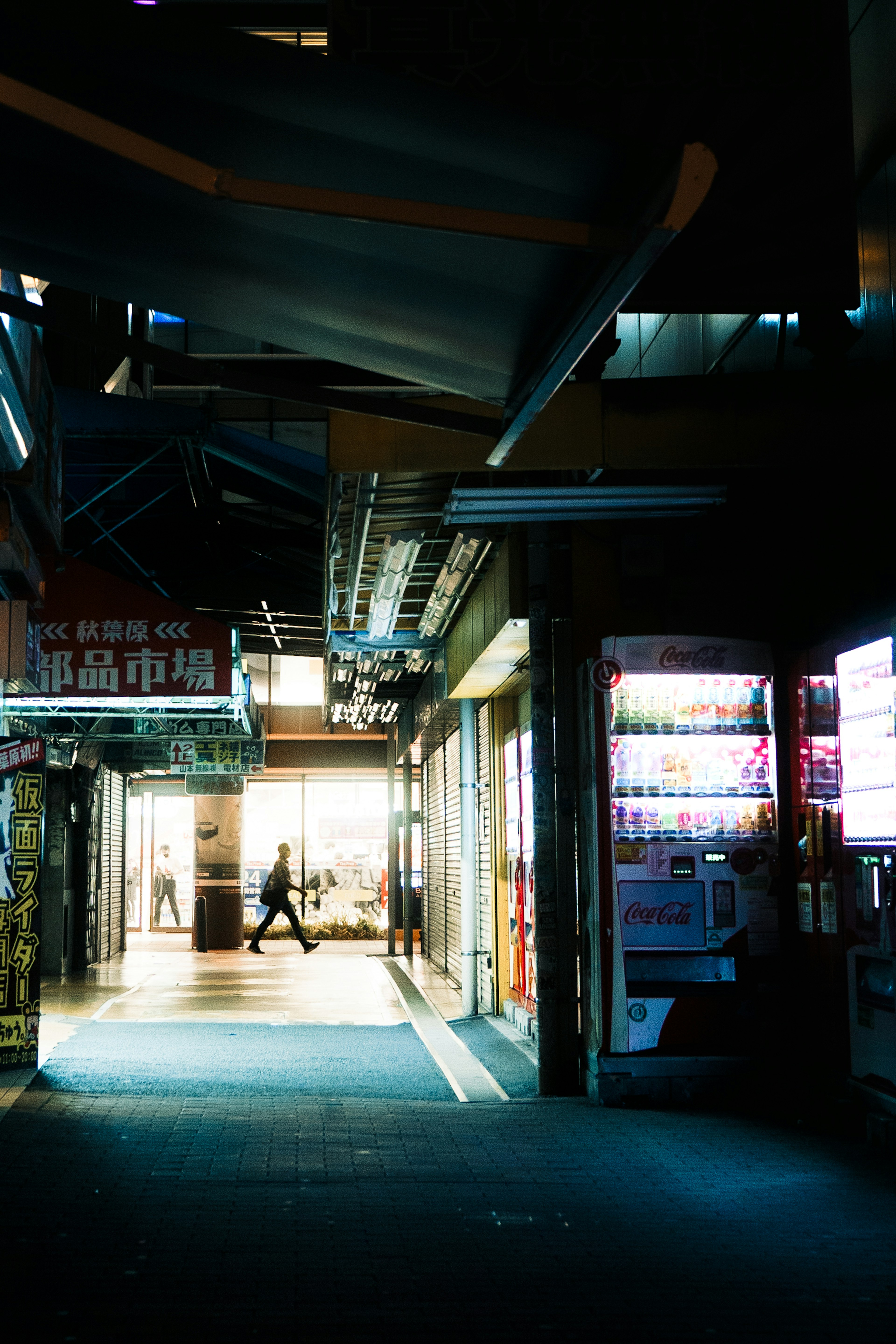 Night scene of a street with a person walking Brightly lit shop and dark alley contrast