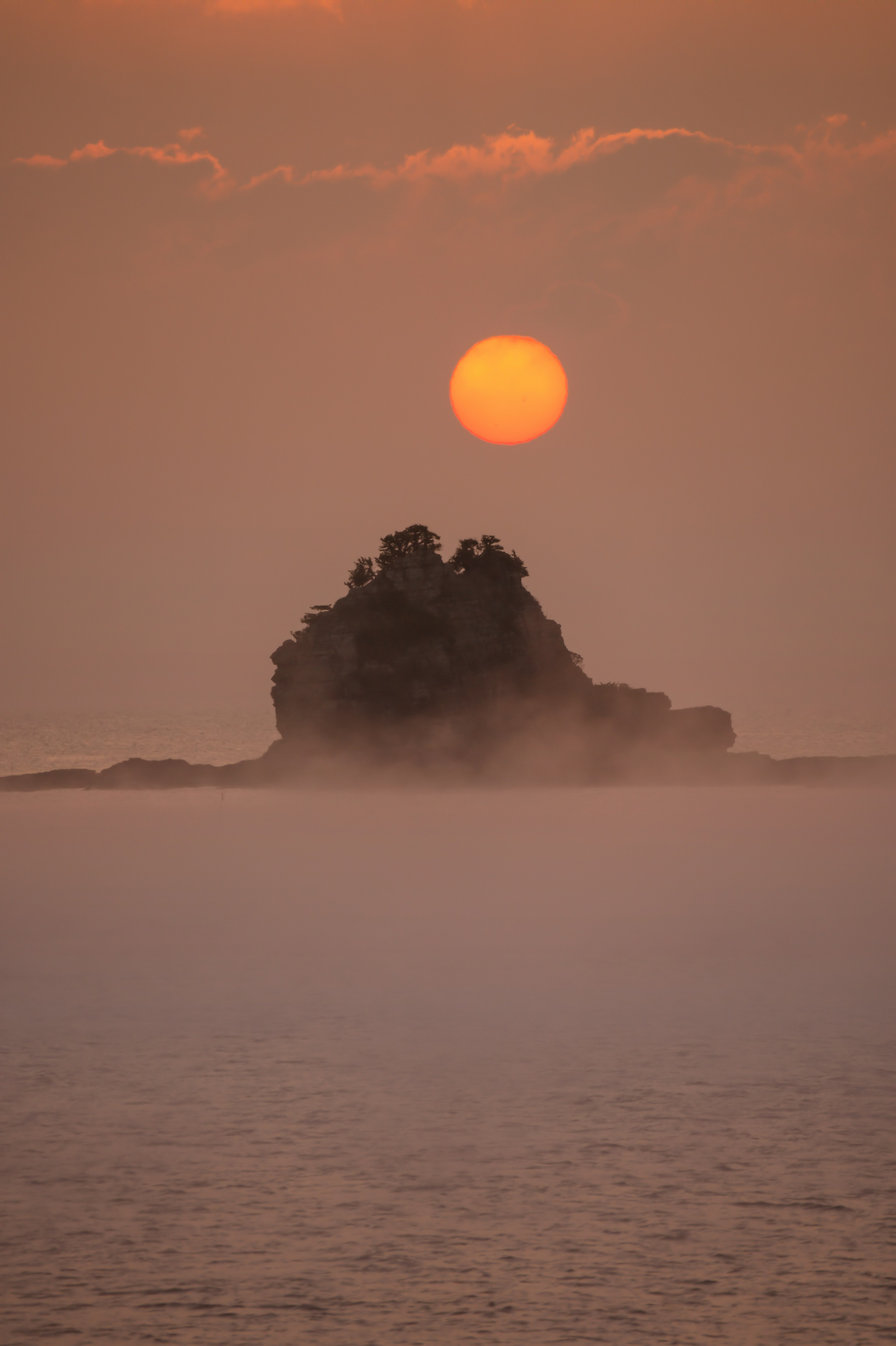 Eine einsame Insel im Meer bei Sonnenuntergang mit einer großen orangefarbenen Sonne