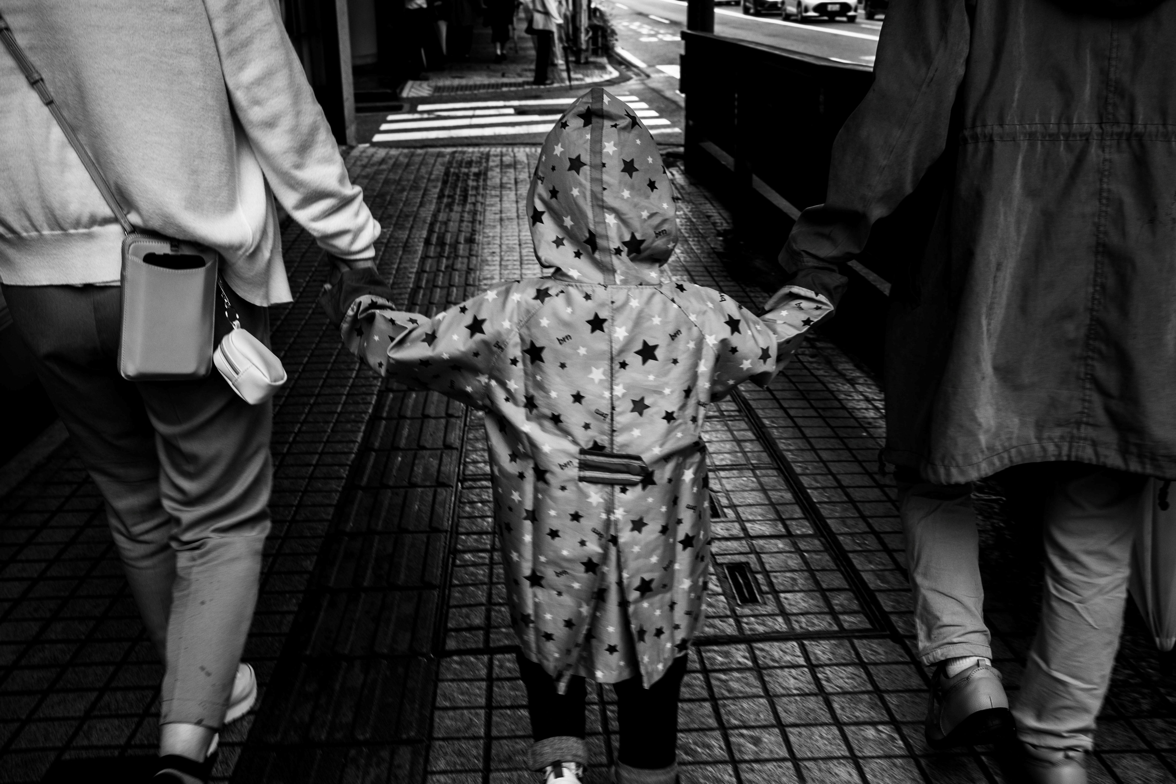 Black and white photo of a child in a raincoat holding hands with parents while walking