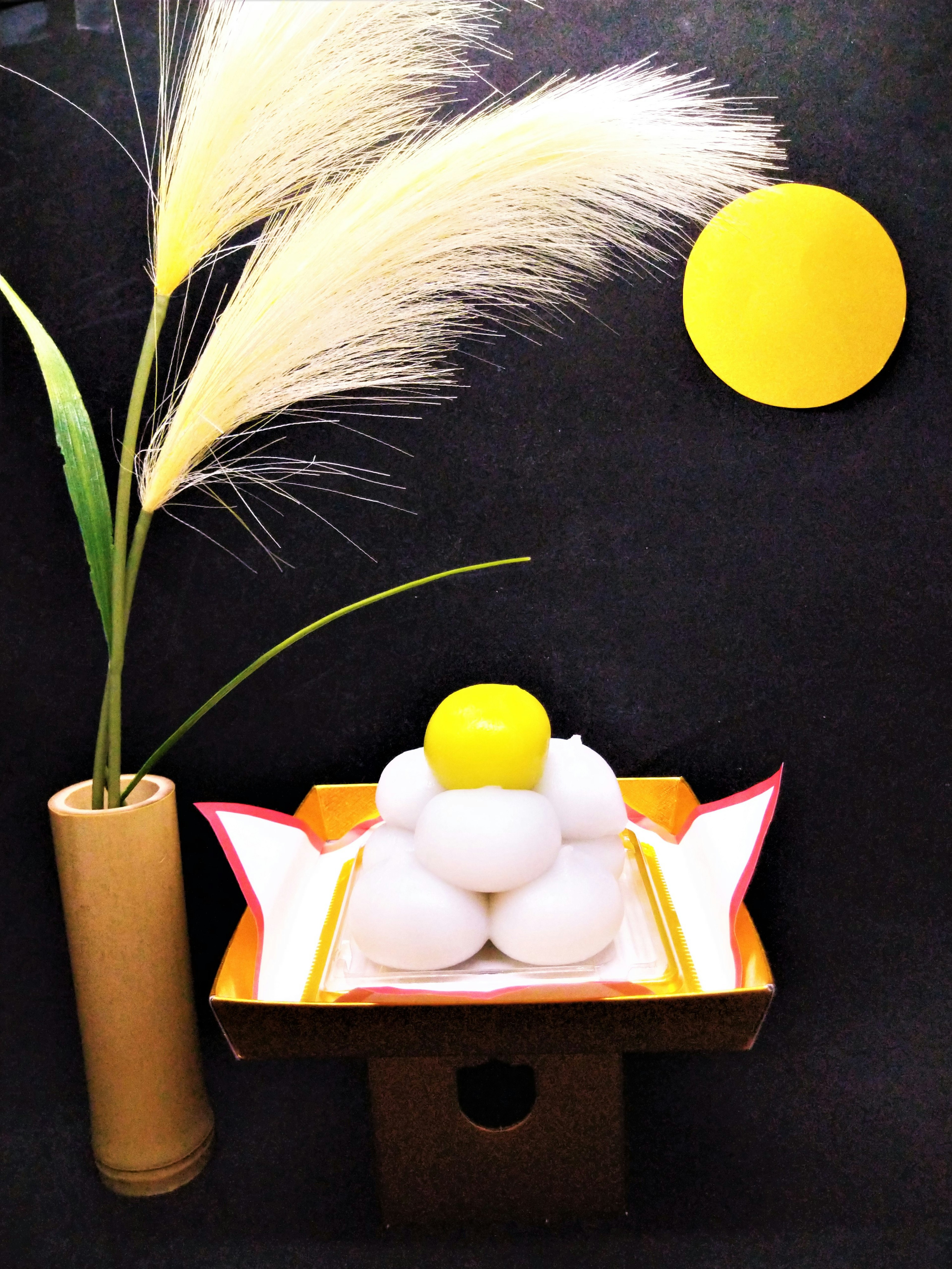 Decorative plate with stacked white rice cakes topped with yellow paste beside a flower arrangement against a simple background