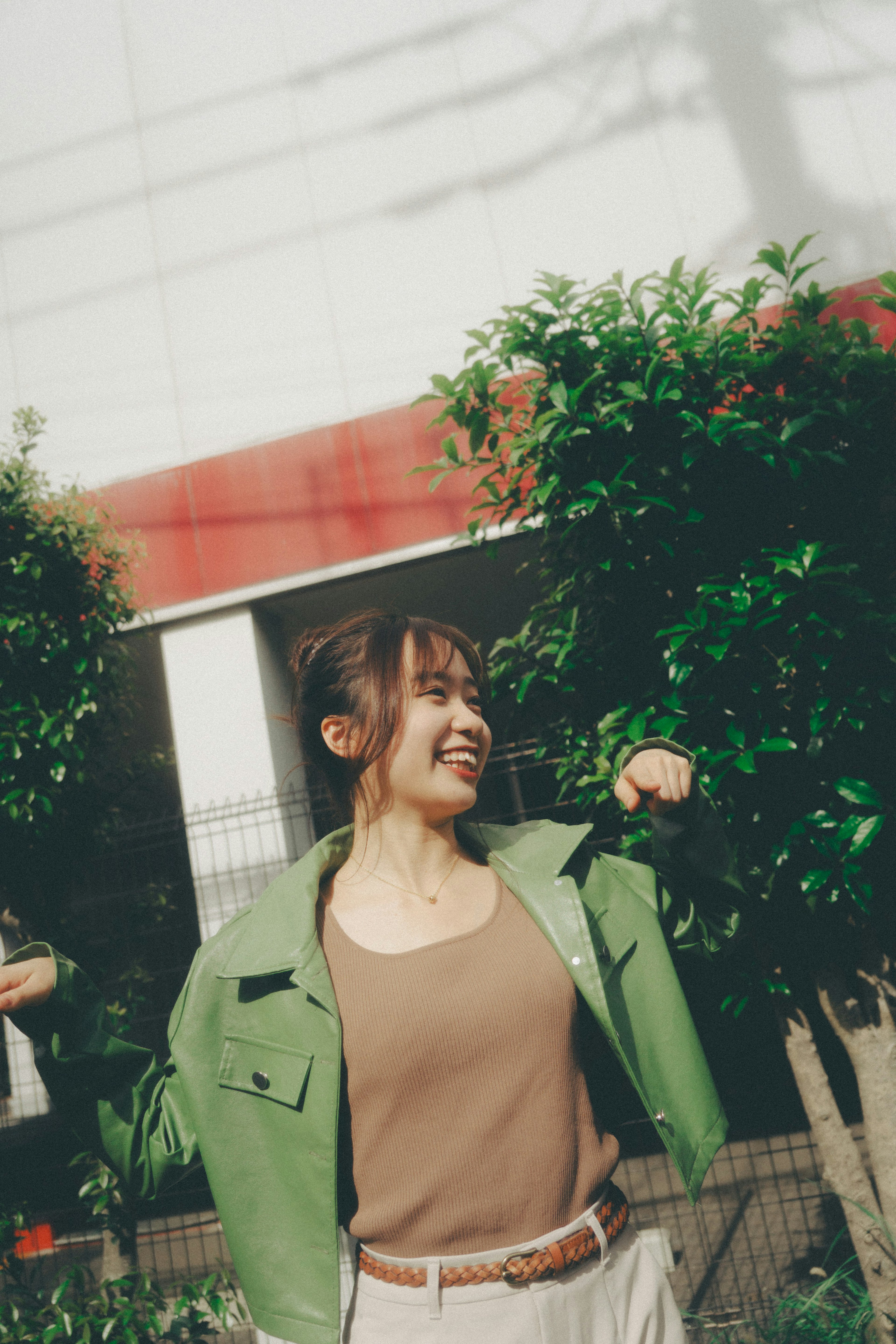 Una mujer sonriente con chaqueta verde posa al aire libre con vegetación de fondo