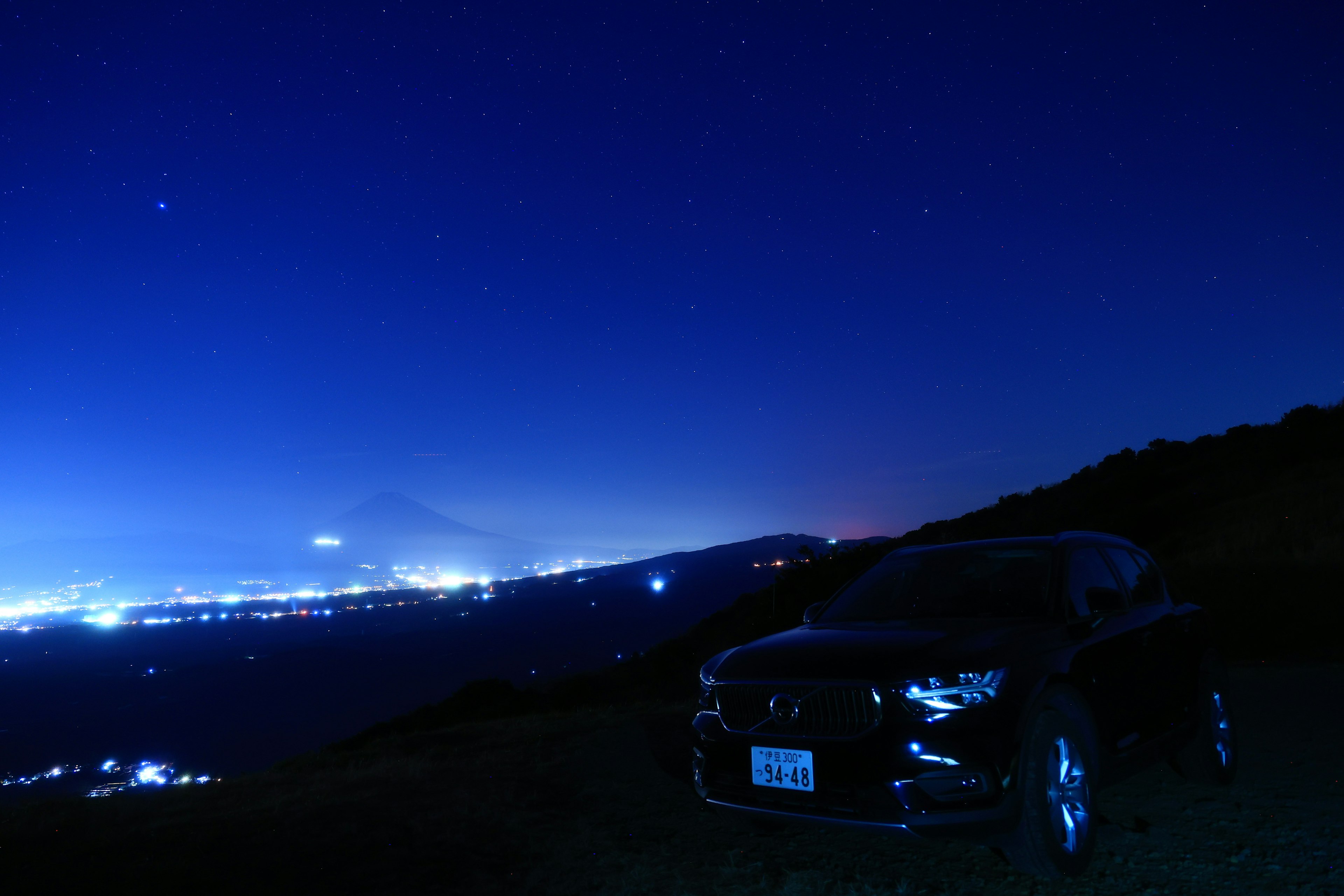 A black car parked on a hill under a starry night sky