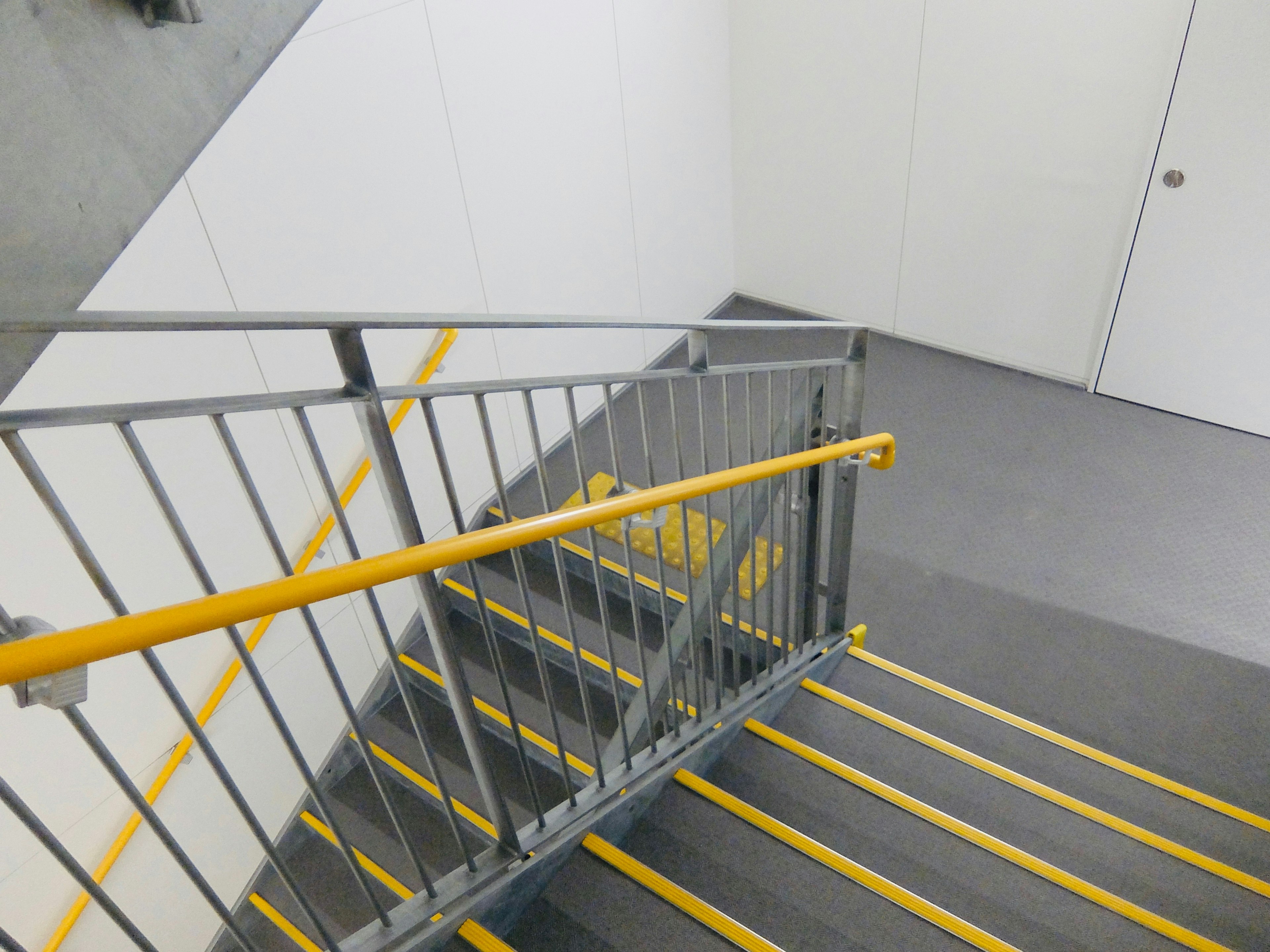 Interior staircase with a yellow-striped step and handrail