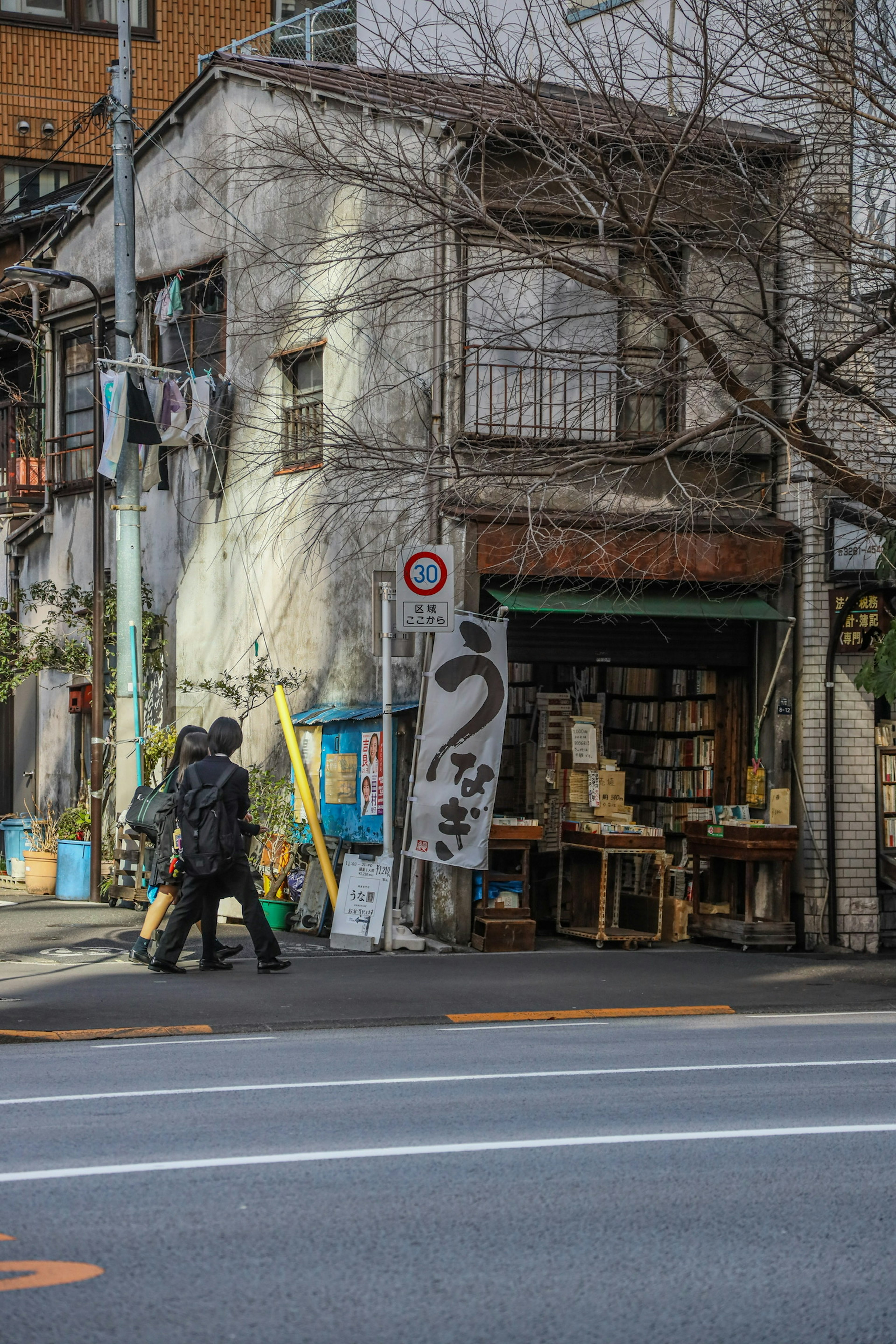 Dua orang berjalan melewati bangunan tua dengan papan toko buku