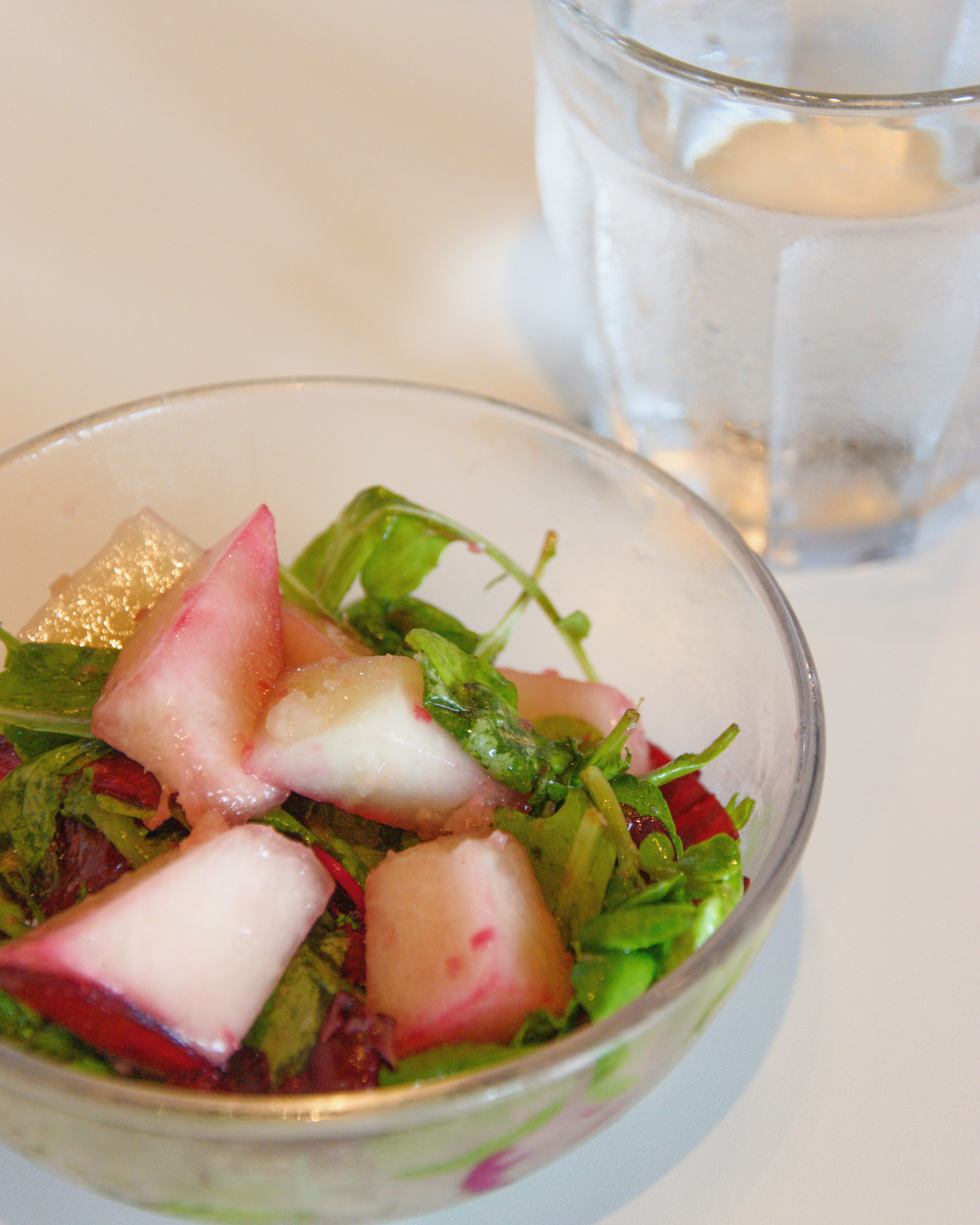 Salade fraîche dans un bol en verre avec des feuilles vertes et des fruits roses