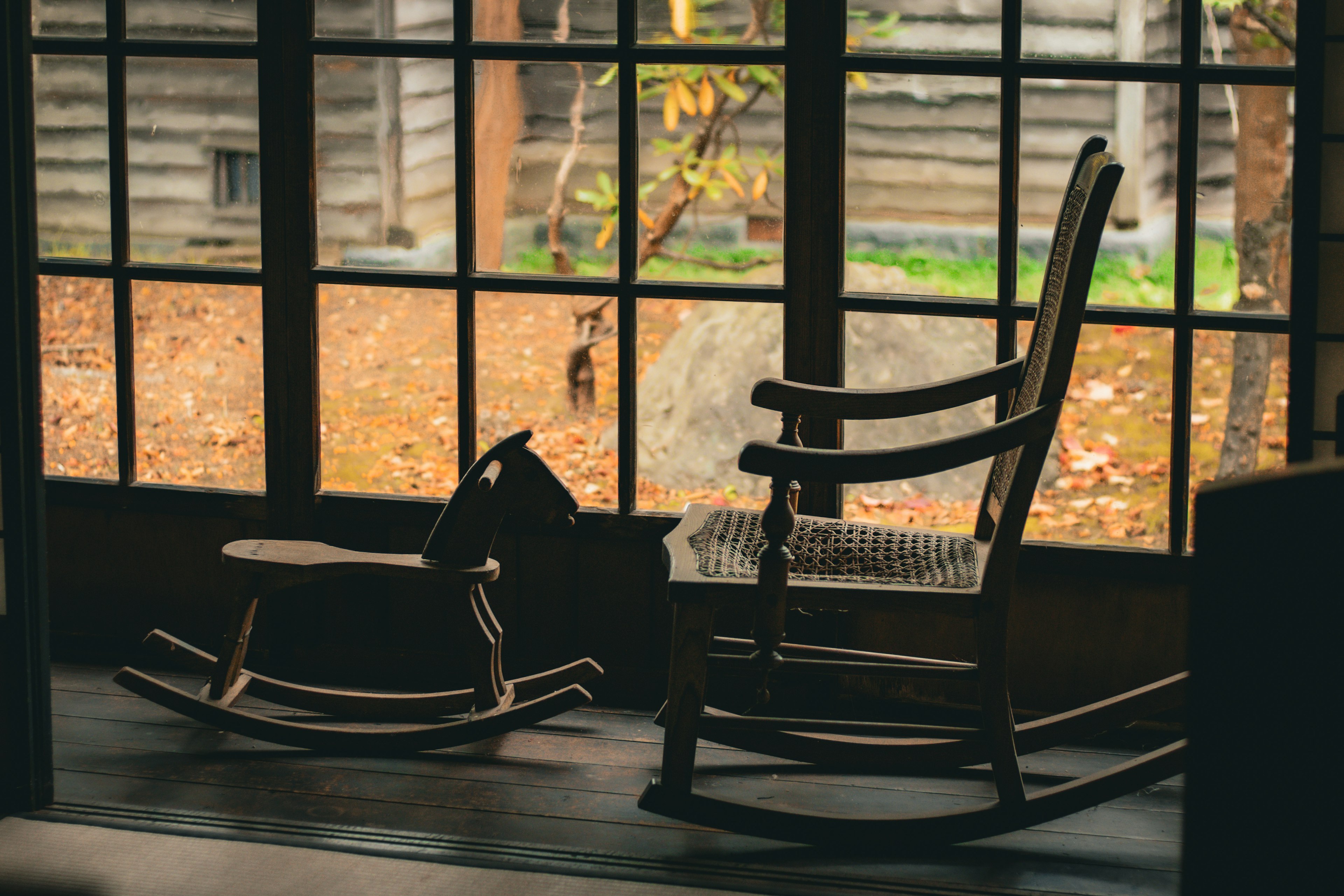 Indoor scene featuring a rocking chair and a wooden rocking horse with autumn leaves outside the window