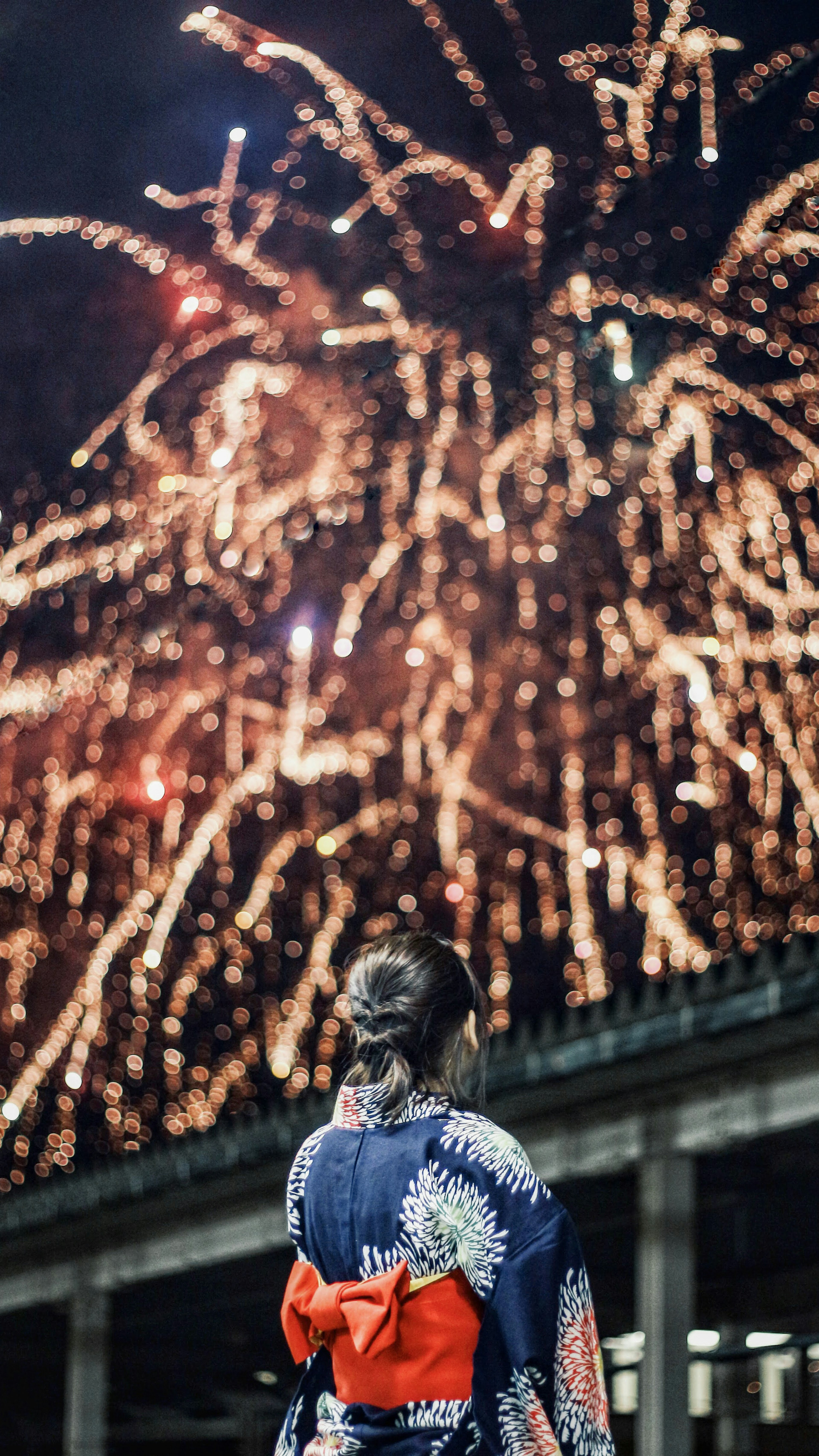 Frau im Kimono schaut nachts Feuerwerk mit einem roten Obi an