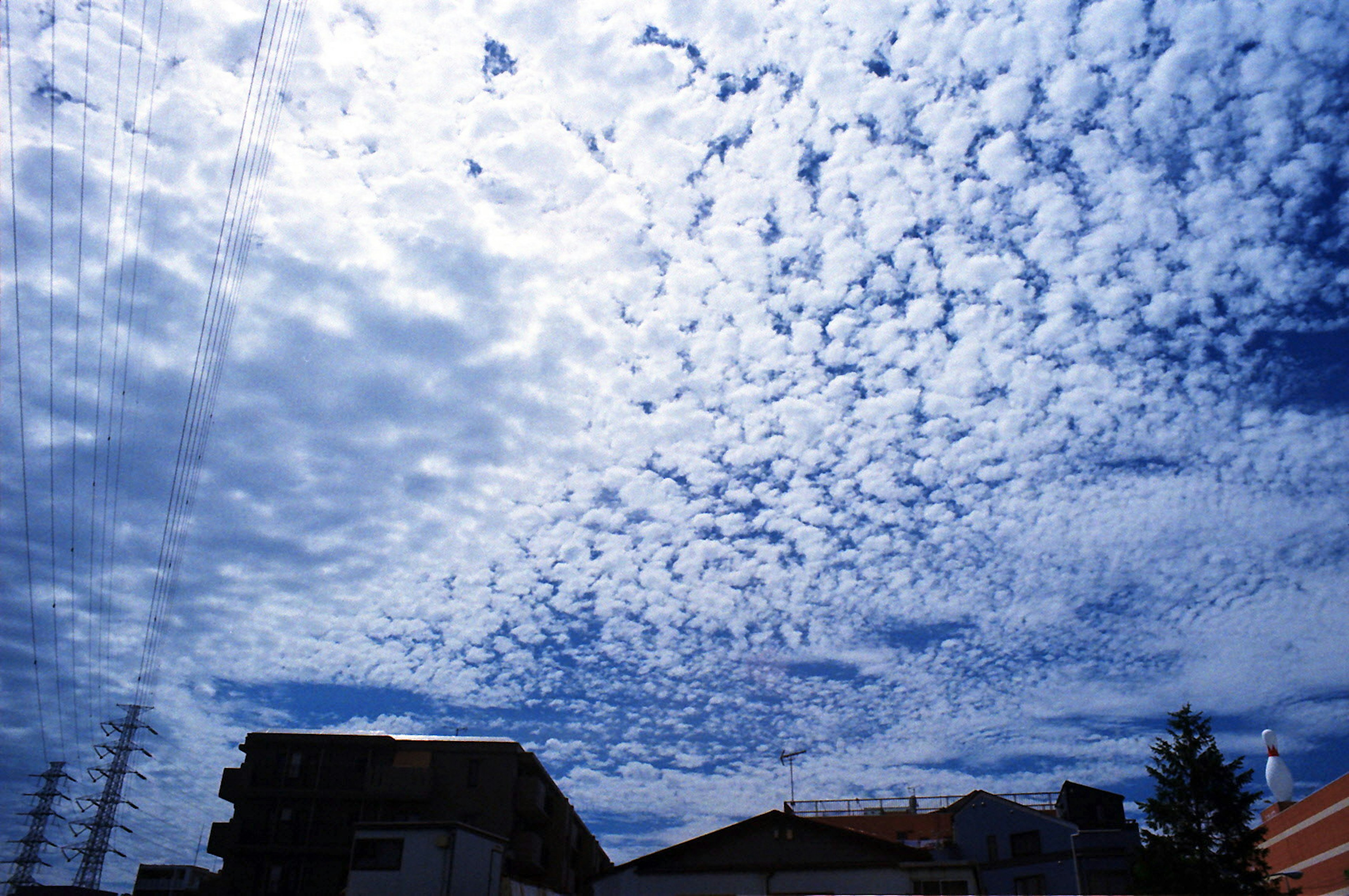 Pattern of white clouds in a blue sky with silhouettes of buildings