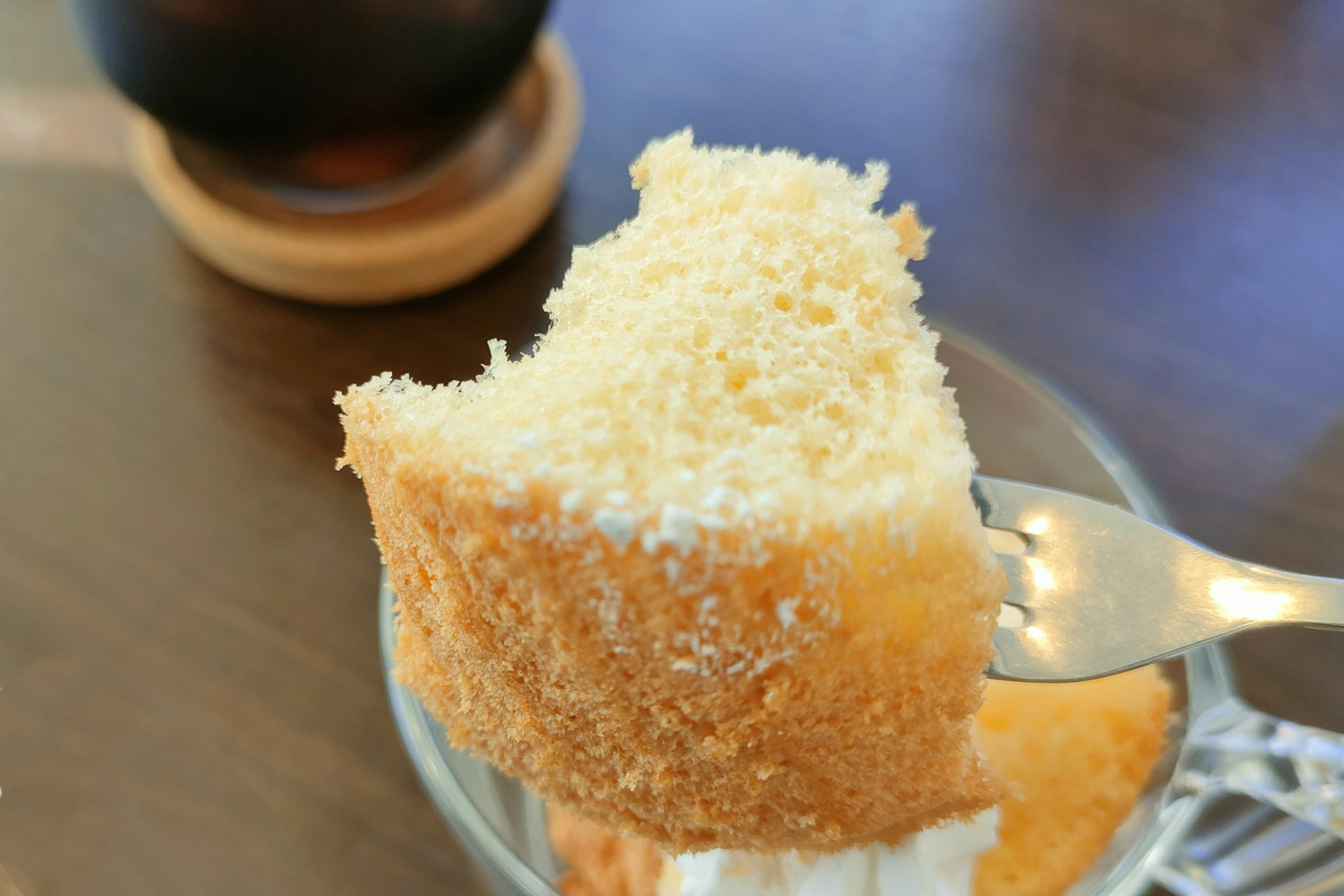 Ein fluffiges Stück Kuchen auf einer Gabel mit einer Teetasse im Hintergrund