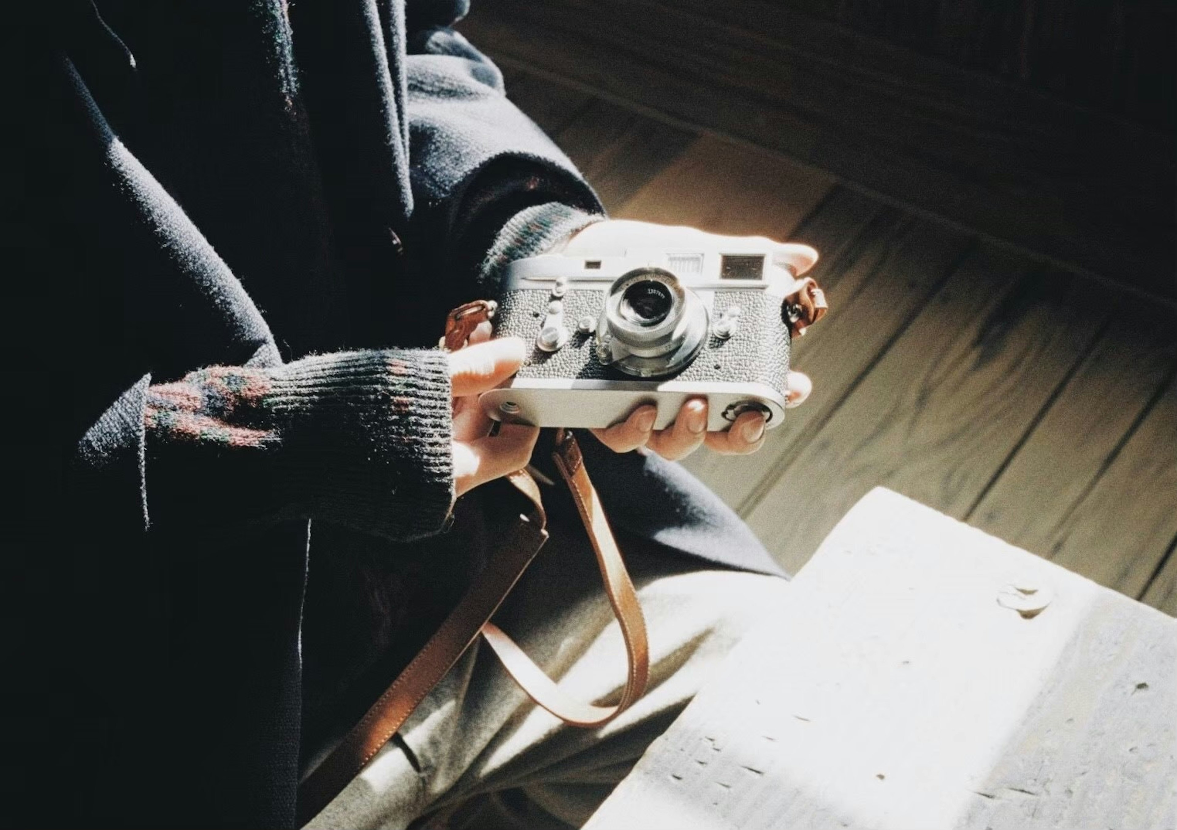 A person holding a camera in their hands sitting on wooden flooring