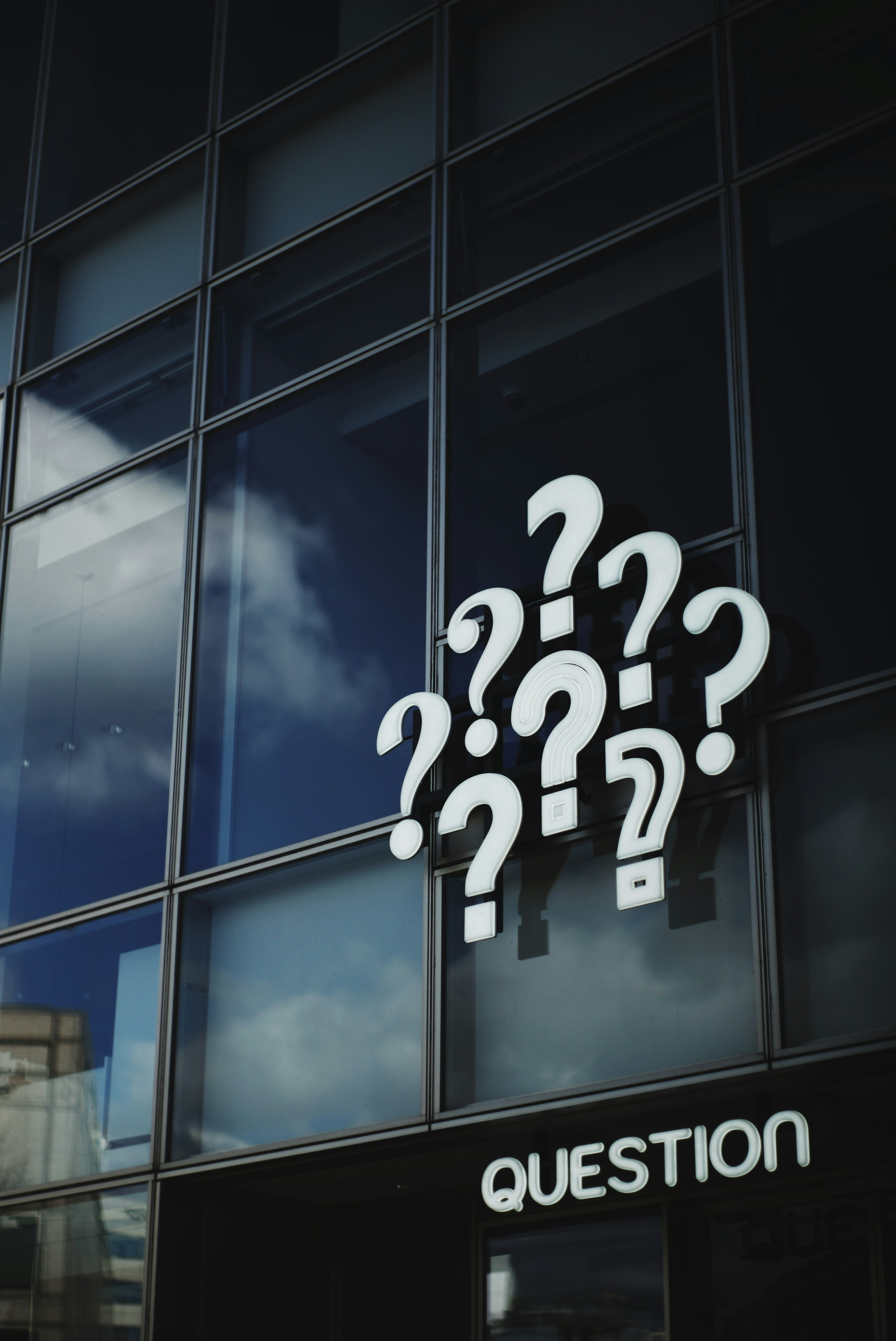 Multiple question mark signs on a glass wall with the word 'QUESTION'