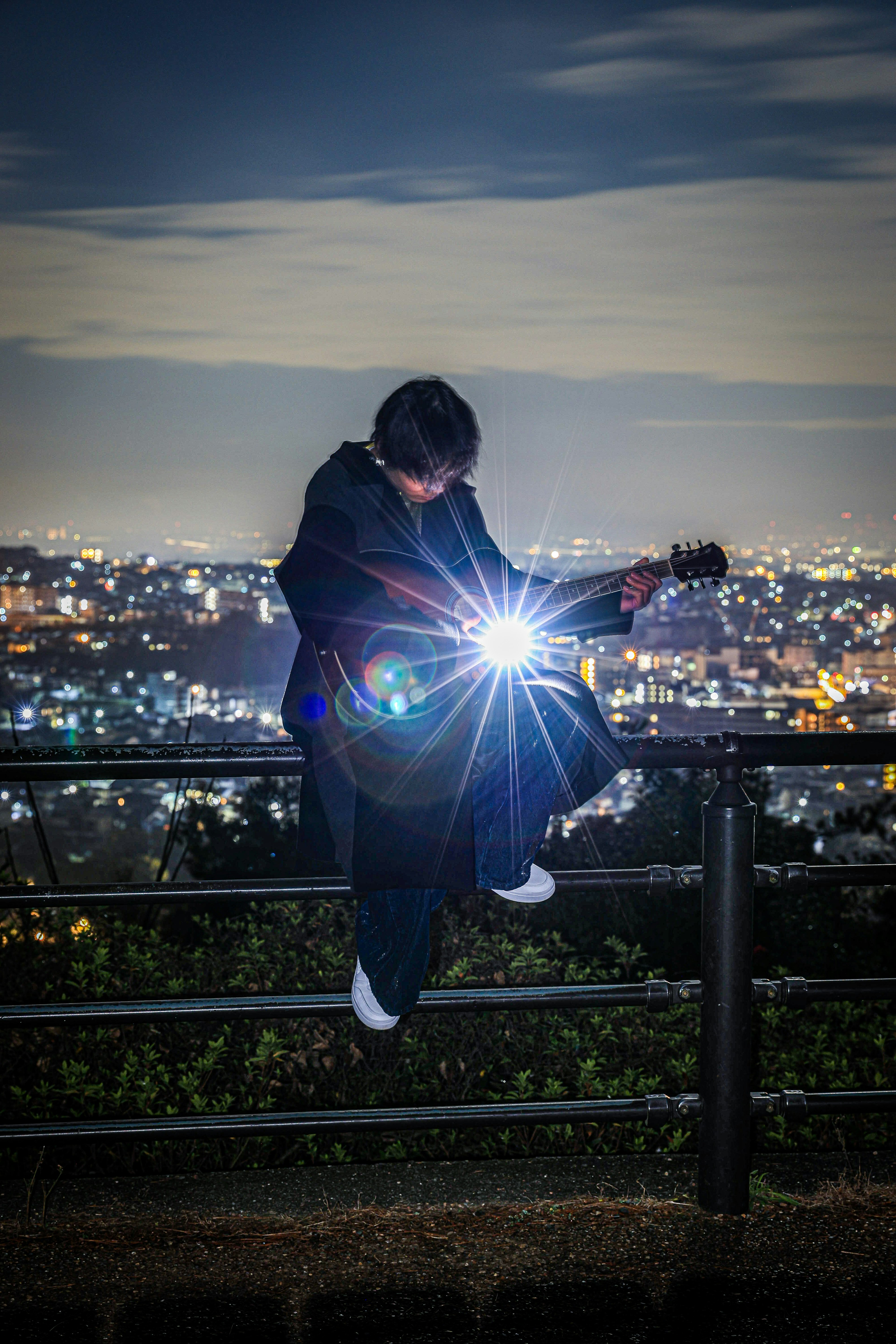 Personne jouant de la guitare avec une lumière brillante sur un paysage urbain nocturne