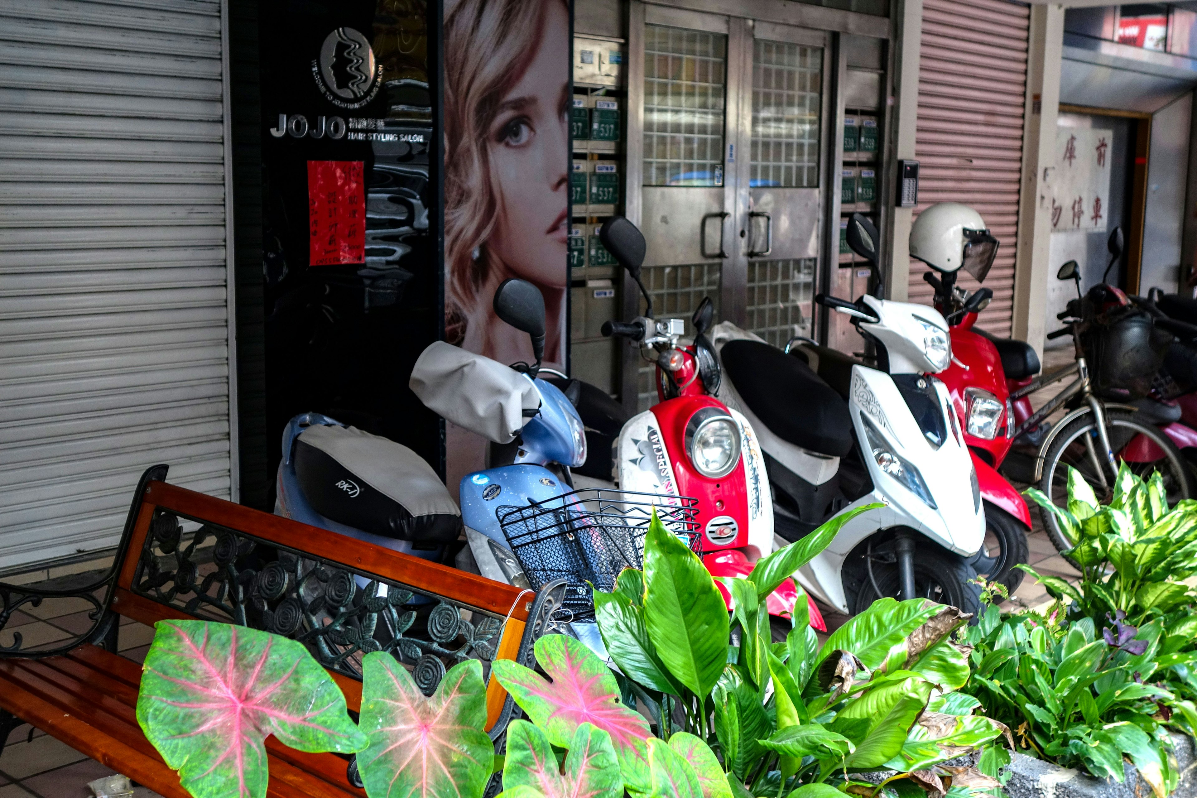 Fachada de un salón de belleza con scooters aparcados y plantas verdes vibrantes