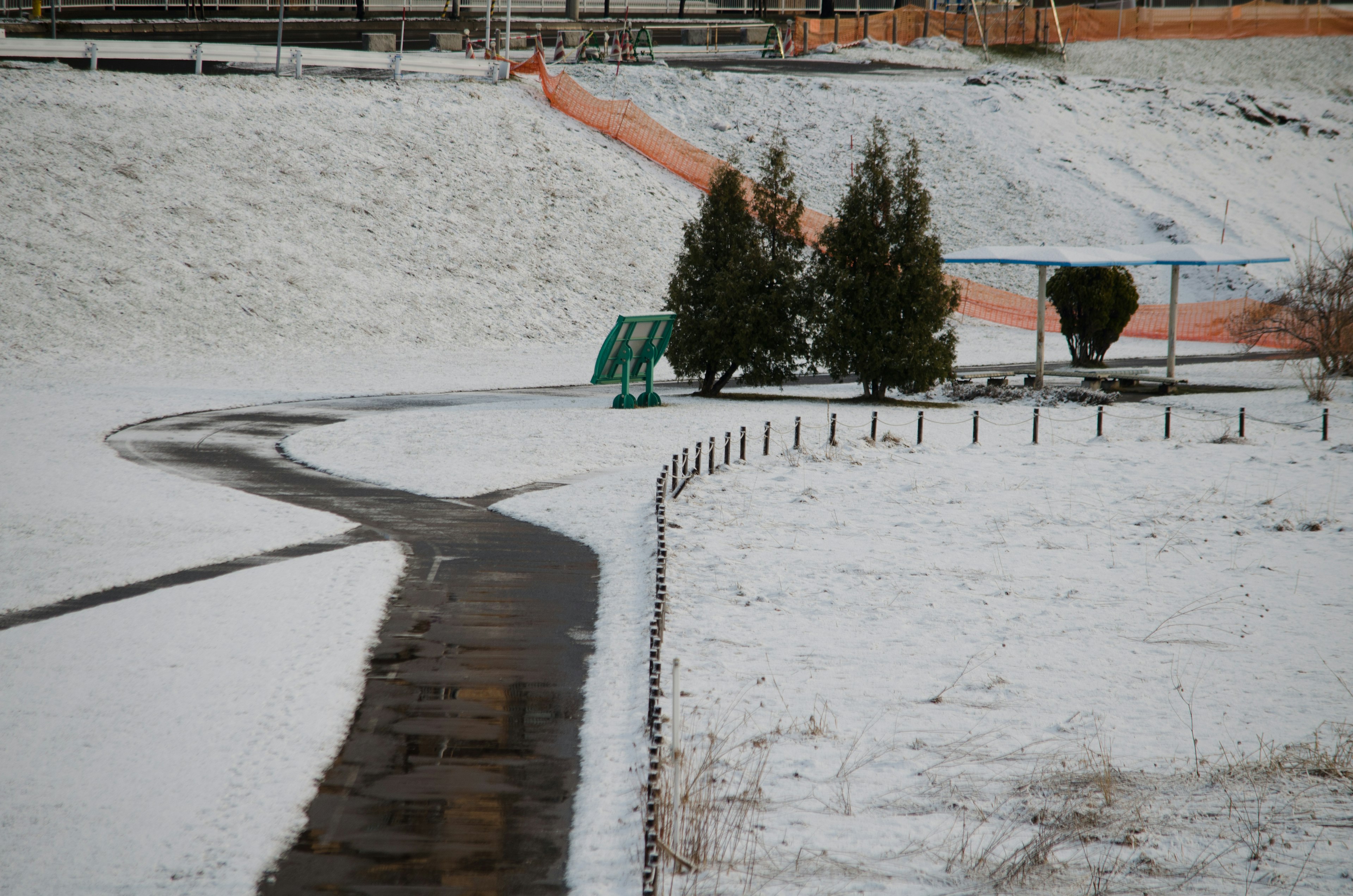 Snow-covered path with green trees and a playground slide