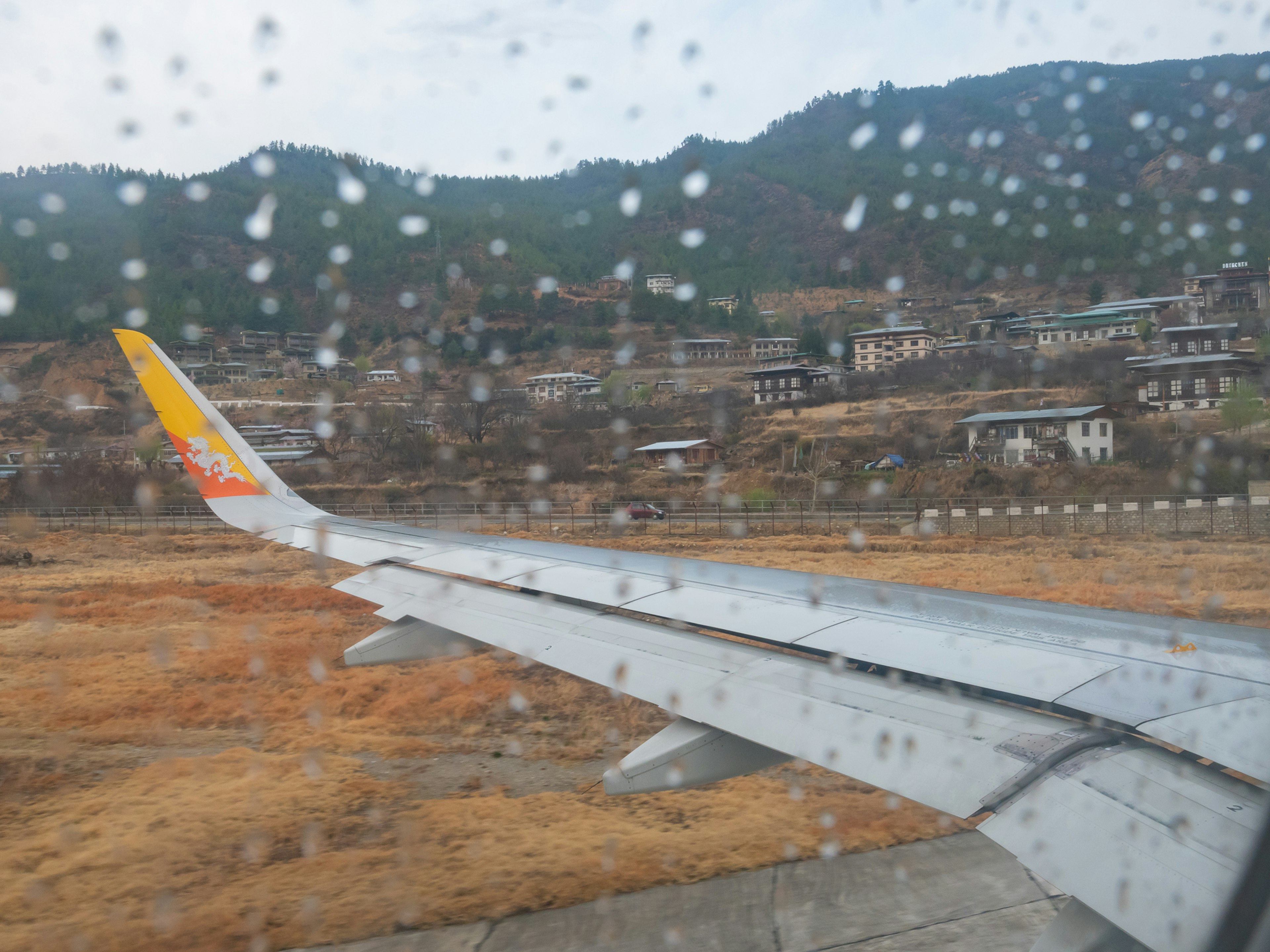 Aile d'avion avec des gouttes de pluie sur la fenêtre montrant un paysage montagneux