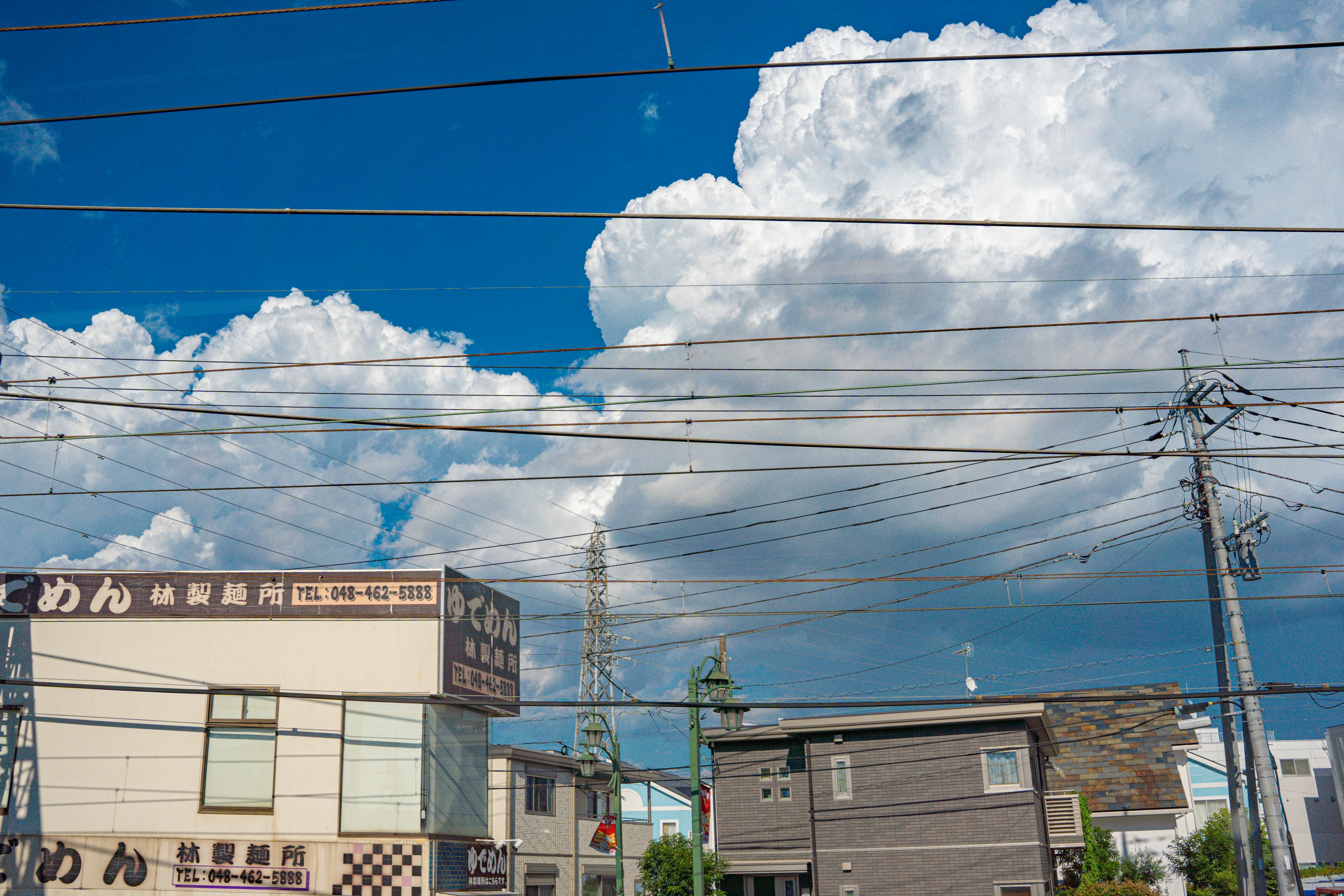 青空と白い雲が広がる風景に、電線と建物が見える