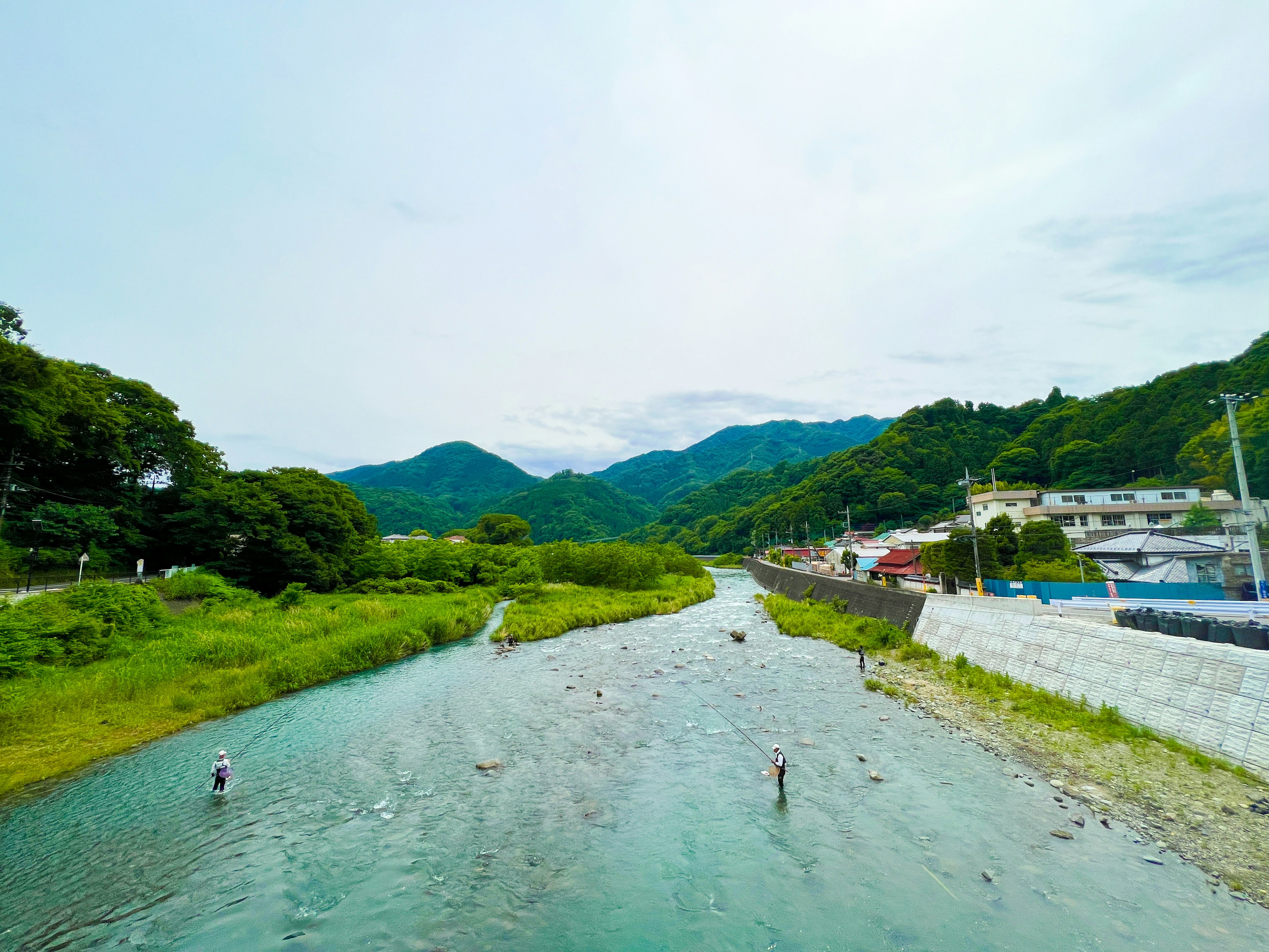 Paisaje de río con personas pescando y montañas al fondo