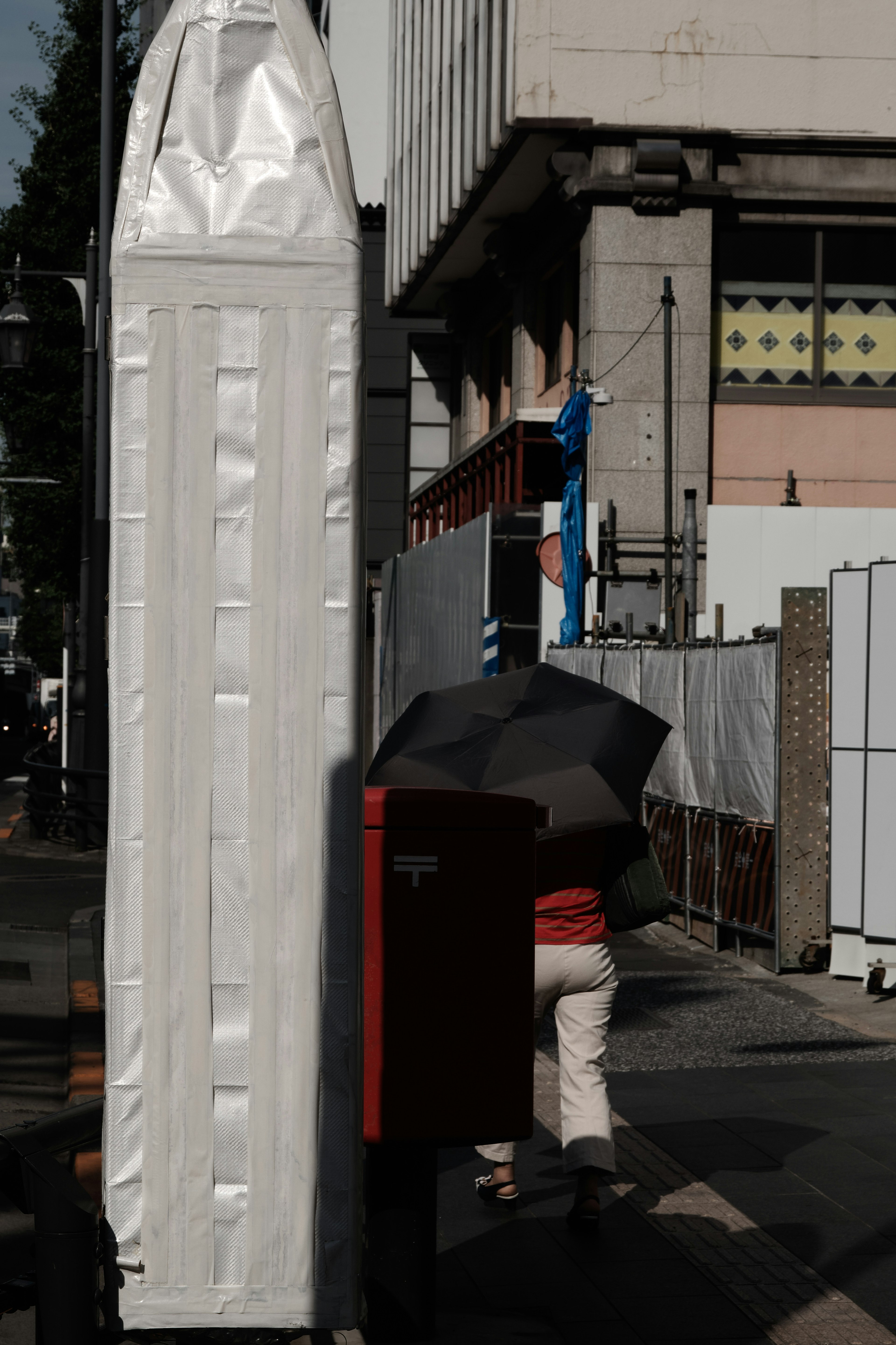 City scene with a white column and a person walking with an umbrella