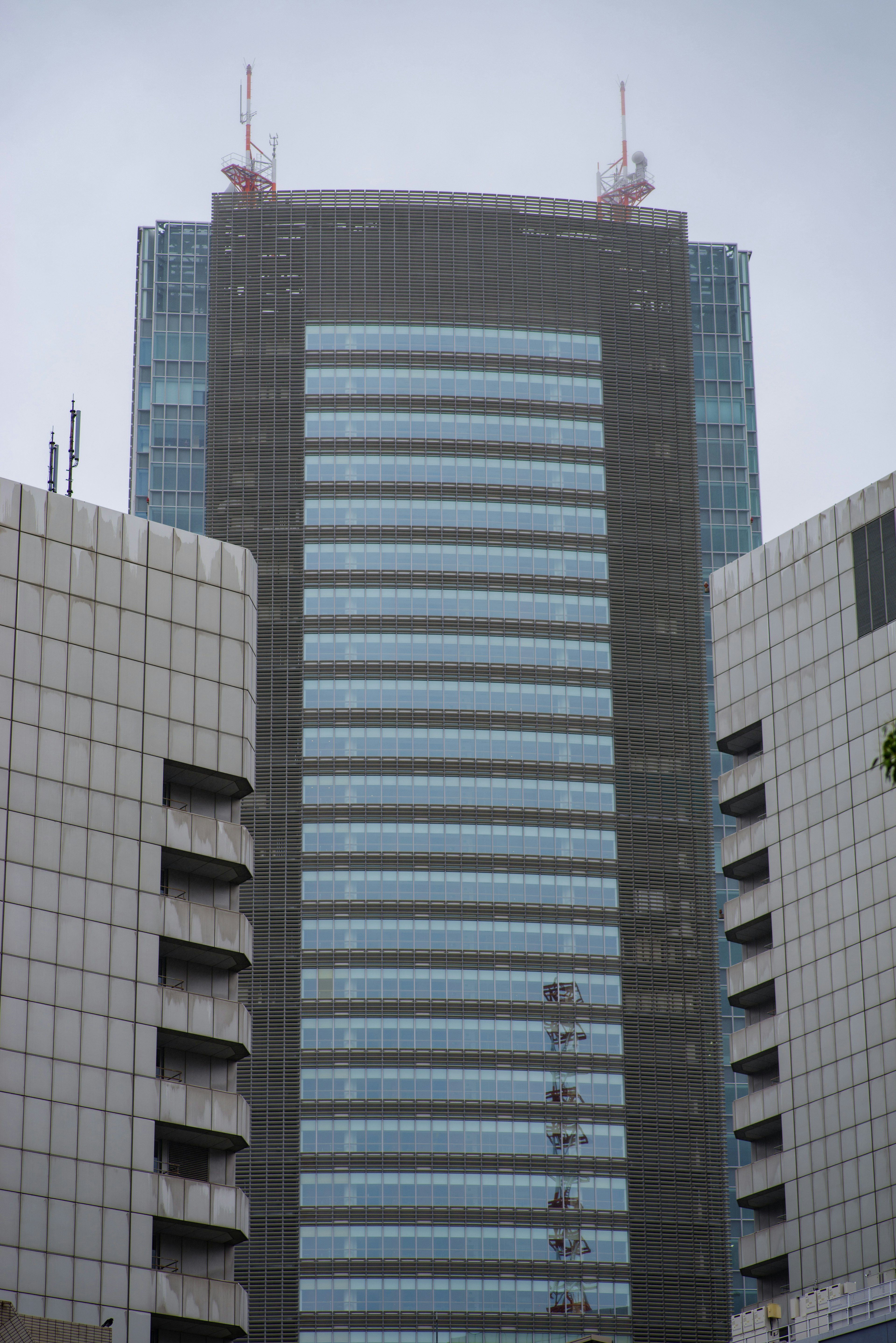 Acercamiento a un rascacielos con fachada gris y ventanas azules con antenas en la parte superior