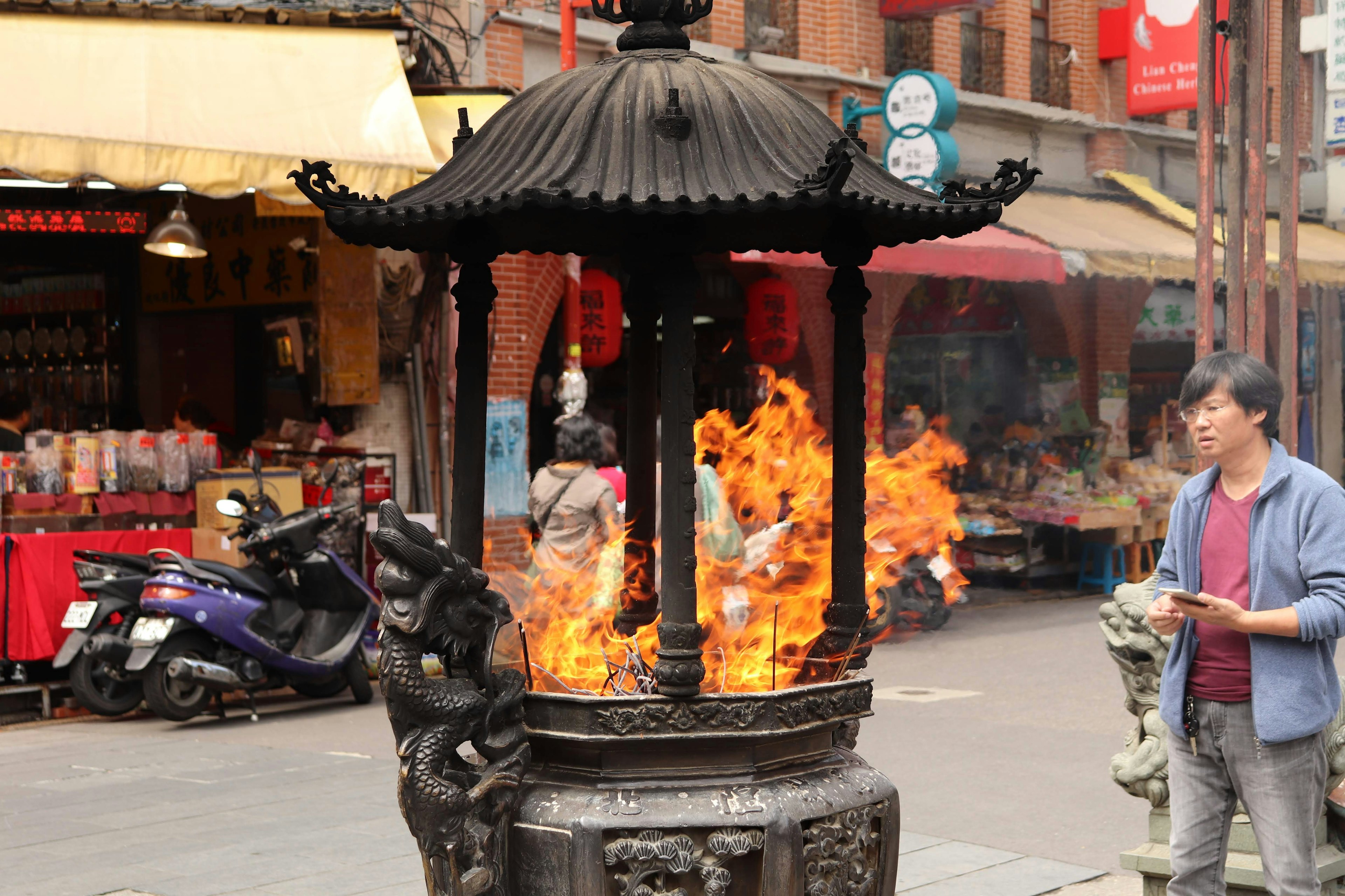 Traditional incense burner with flames and nearby market stalls