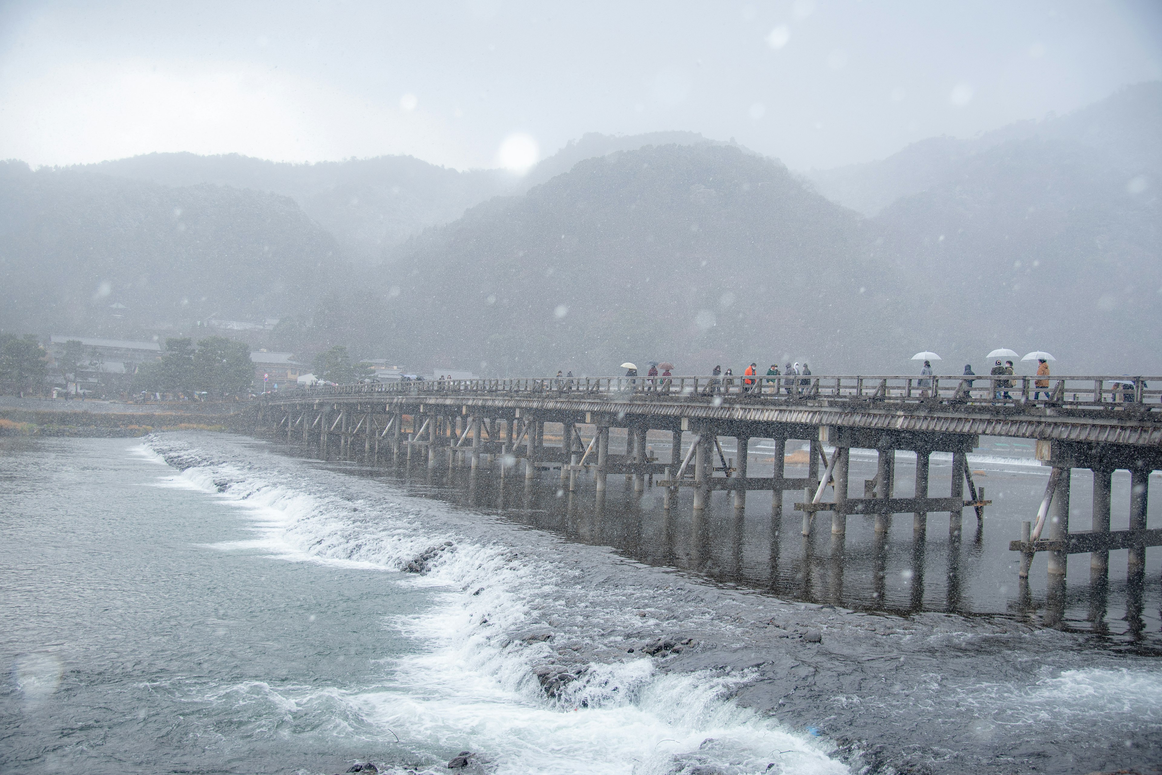 雪の降る中、山に囲まれた桟橋を歩く人々