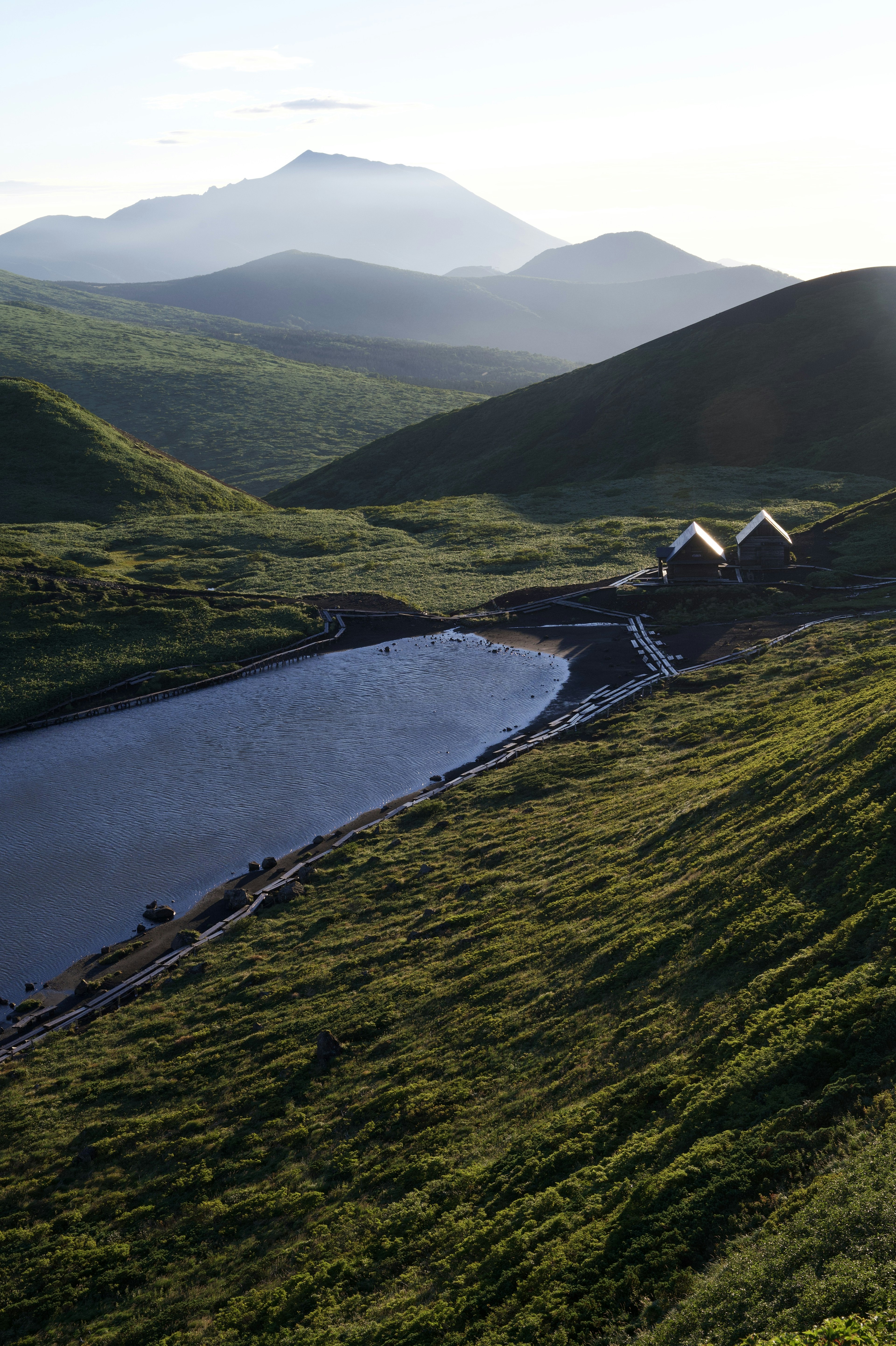 Vue panoramique de montagnes et d'un lac Prairies vertes et cabanes visibles