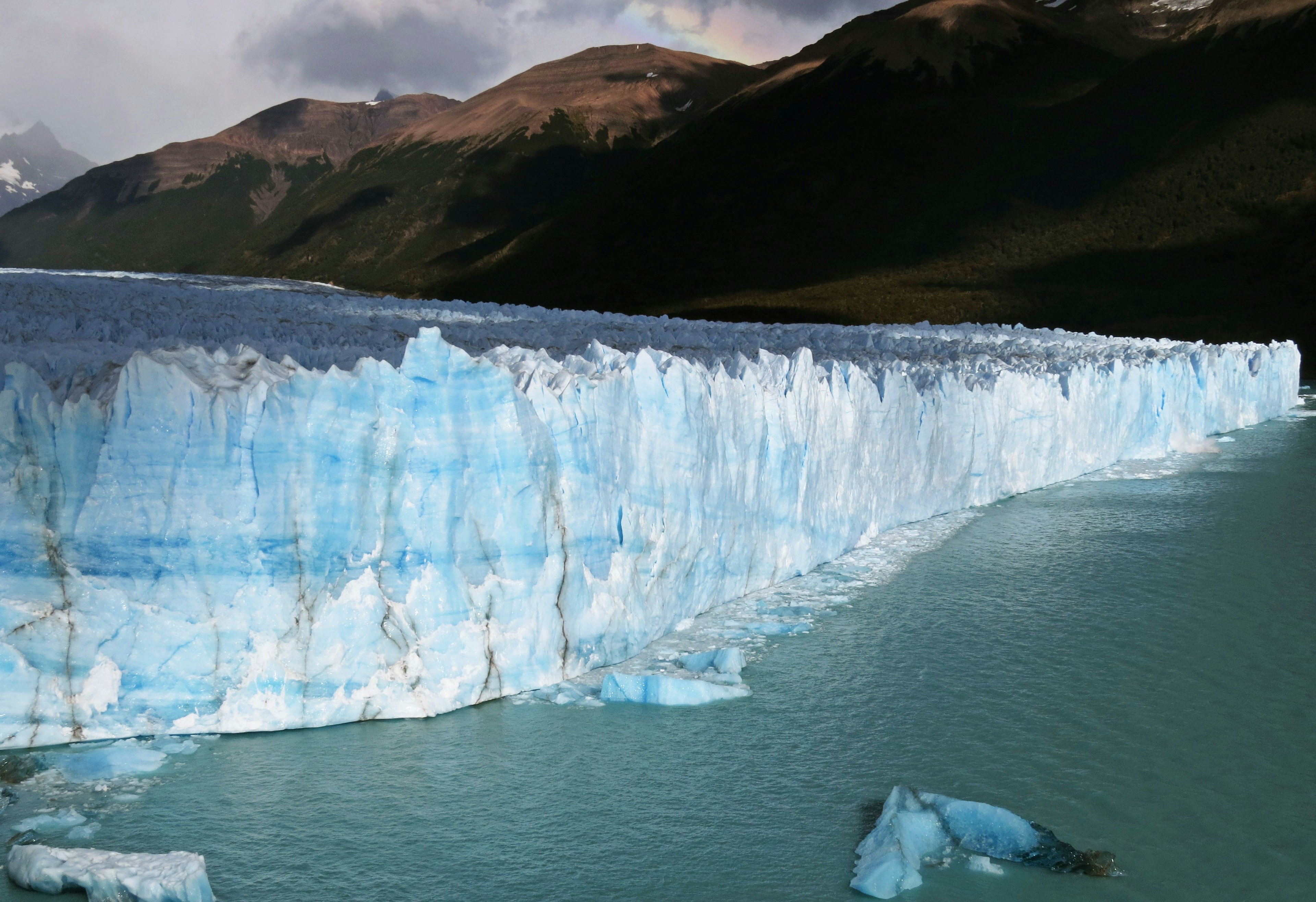 Glacier's blue ice wall facing a lake