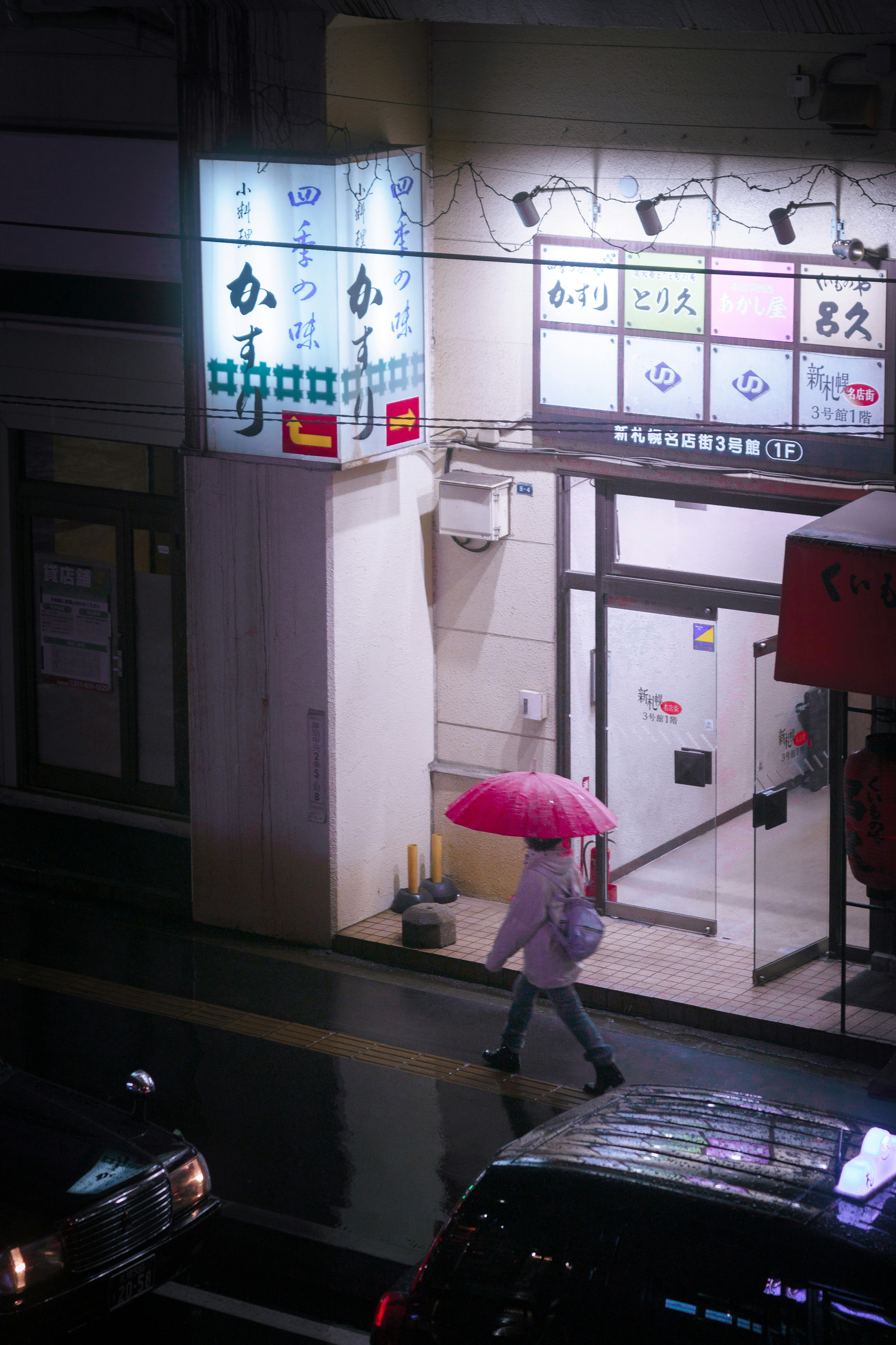 一個人在雨中拿著粉色雨傘走在城市街道上