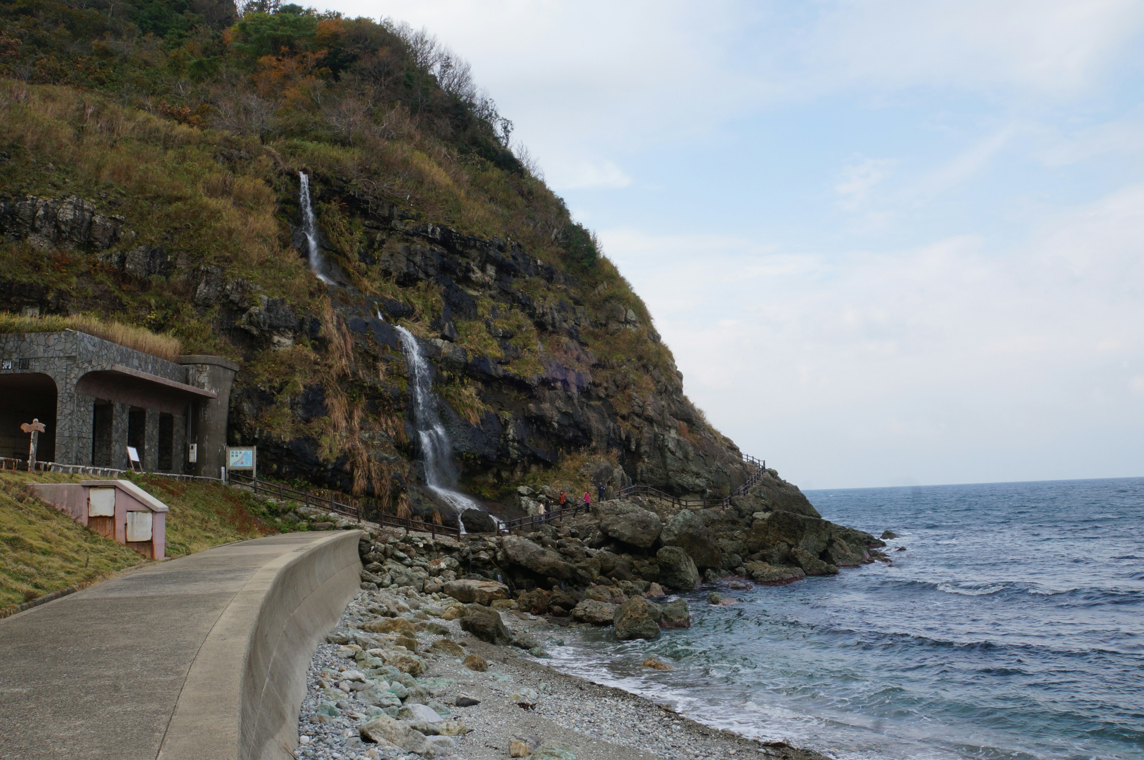 海岸沿いの風景に滝が流れる山の斜面