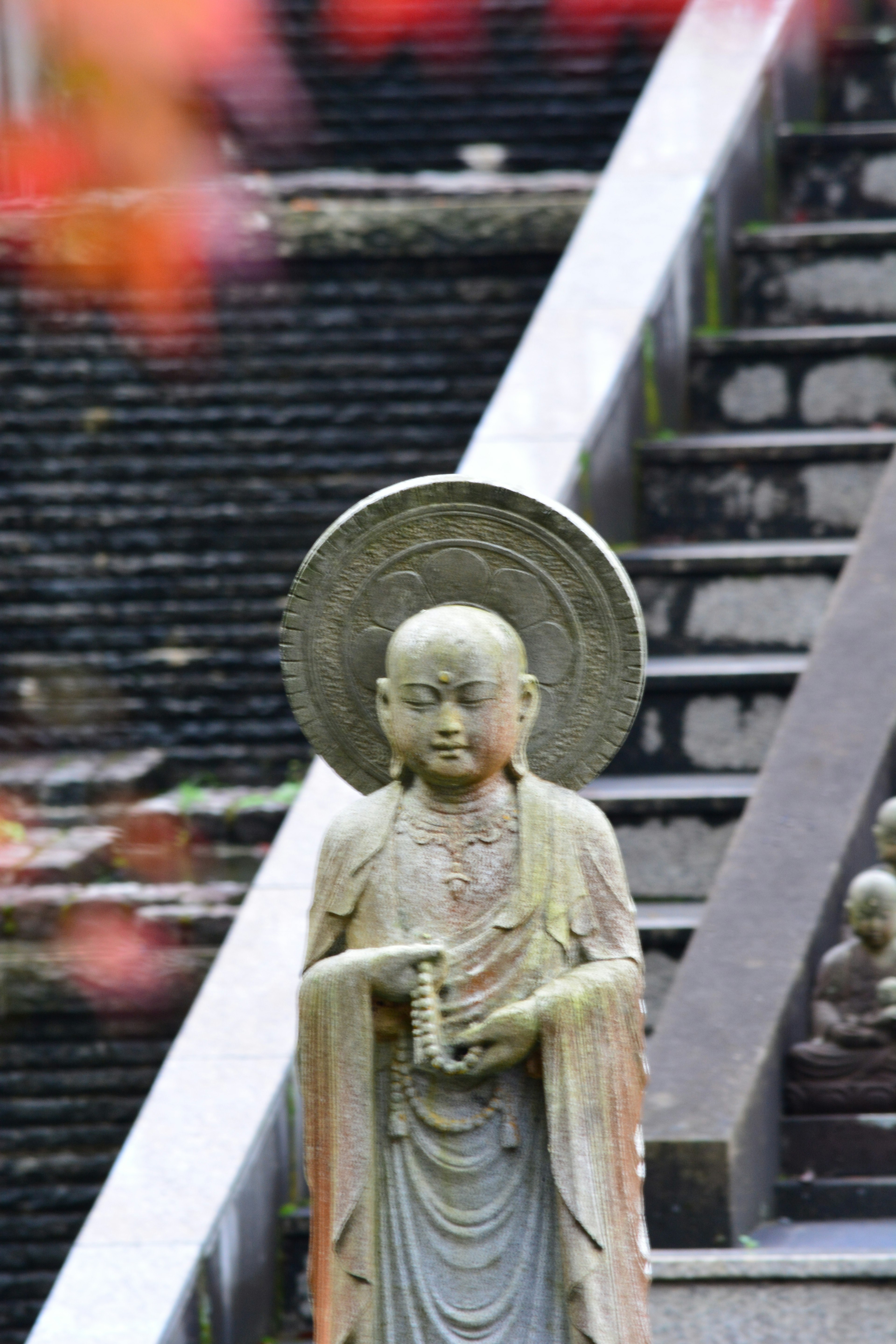 Estatua de piedra de un Buda cerca de escaleras con hojas de otoño al fondo