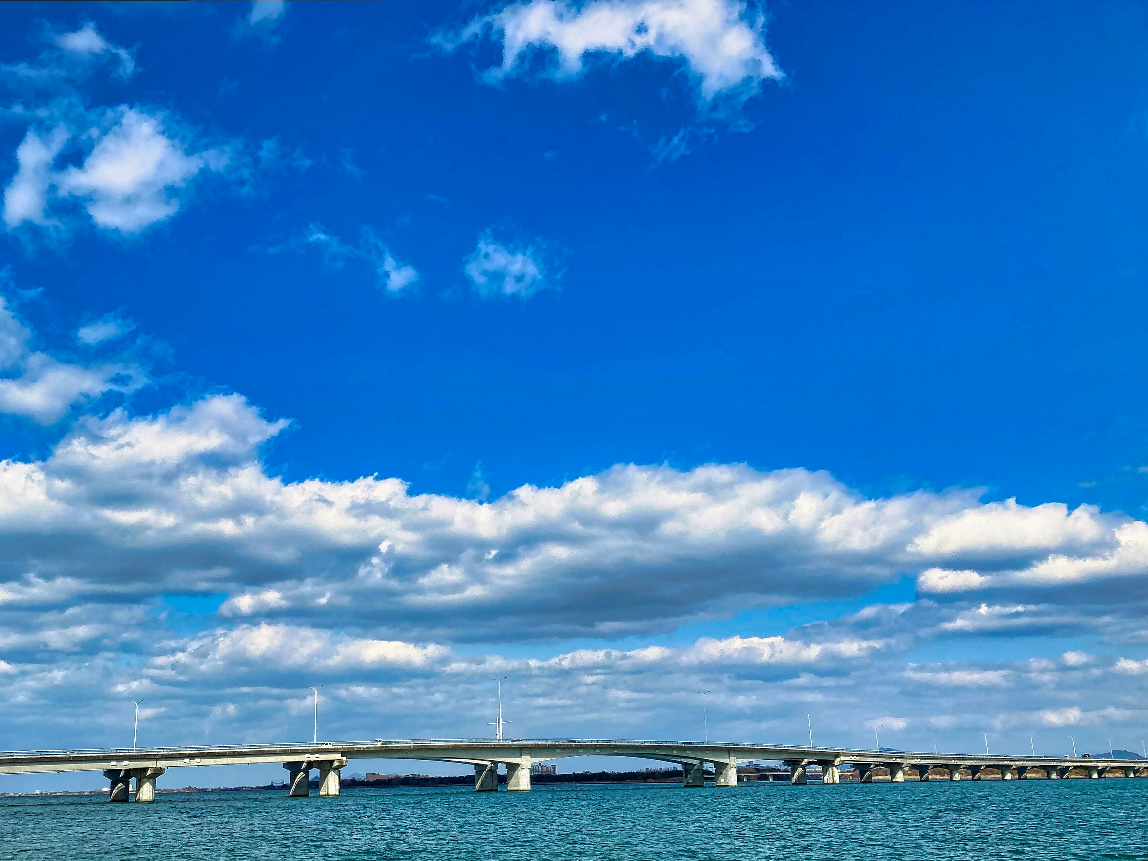 Un long pont s'étendant sur des eaux calmes sous un ciel bleu avec des nuages blancs duveteux