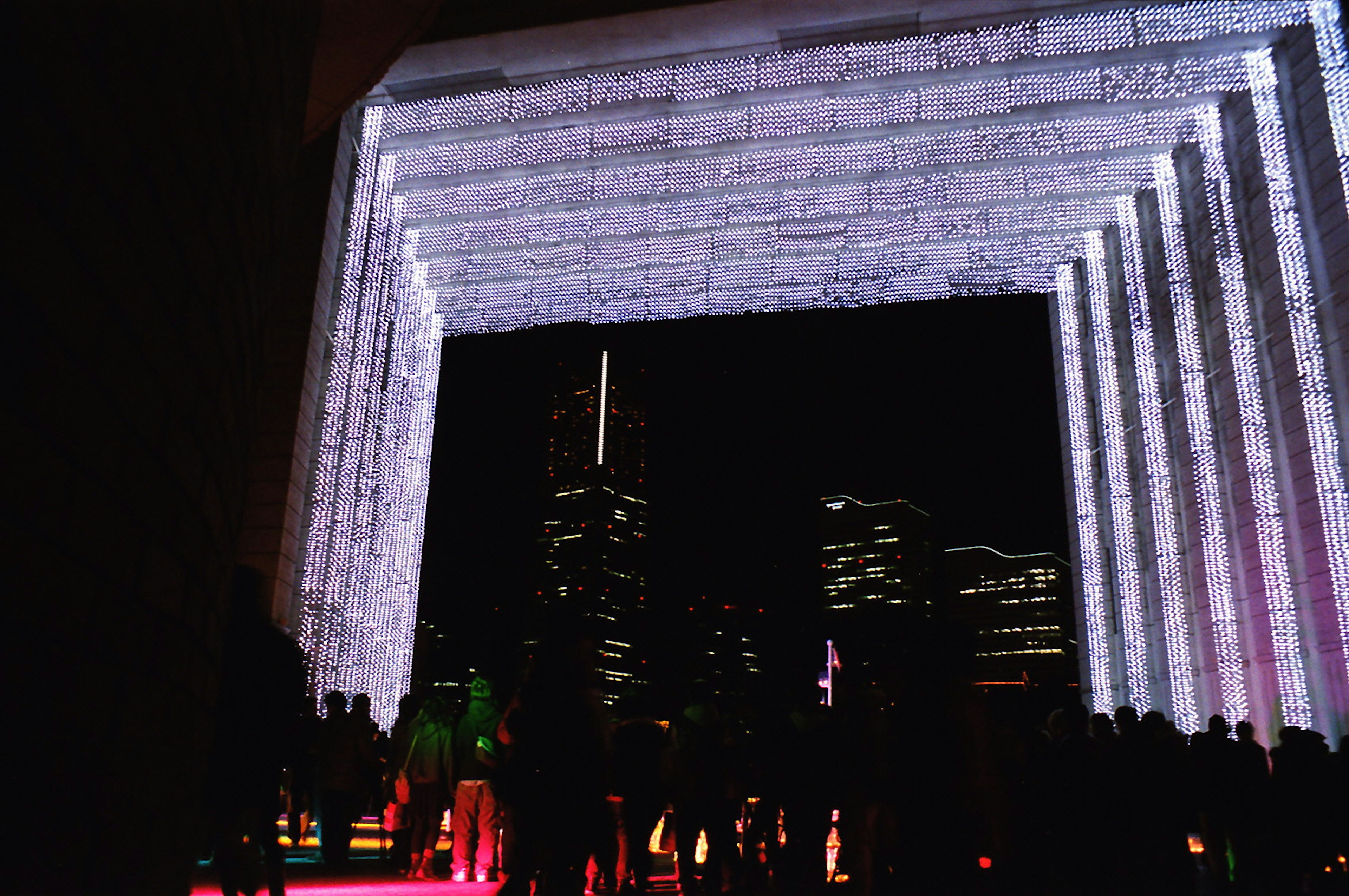 Estructura arqueada iluminada con personas frente a un fondo de ciudad nocturna